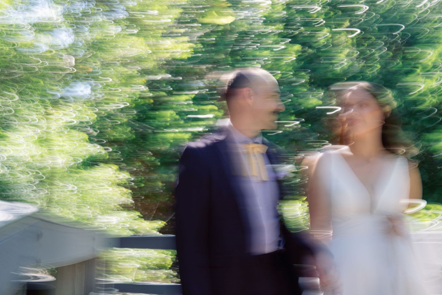 Motion-blurred photograph of figures walking through a lush green garden setting.