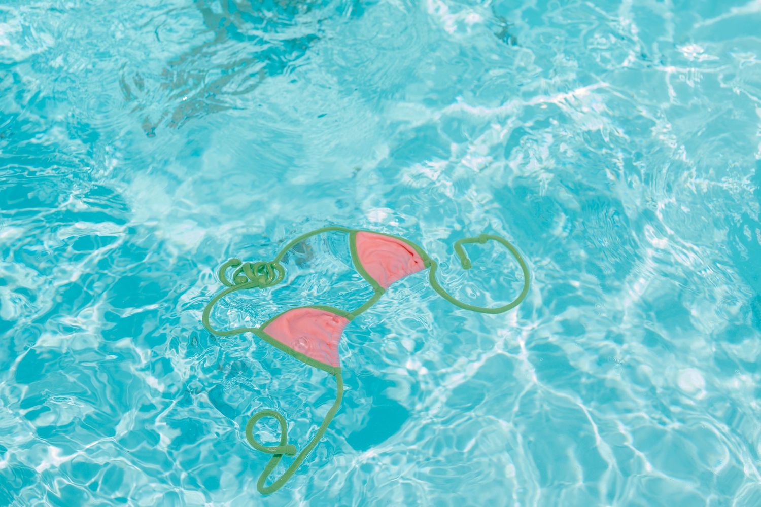 Pink bikini top floating in a clear turquoise swimming pool with rippling water reflections.