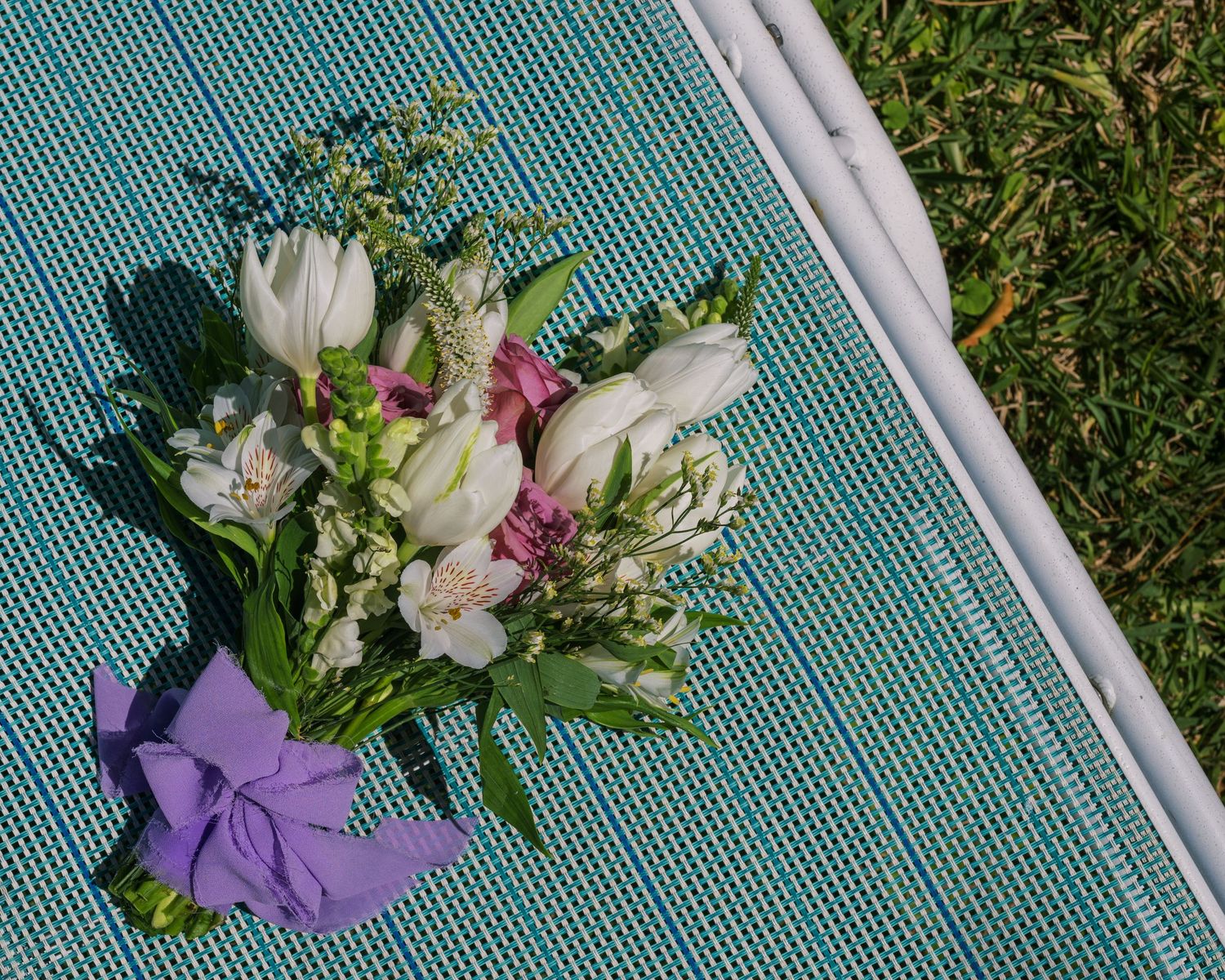 Fresh white and pink alstroemeria flowers arranged on a turquoise surface against green grass background.