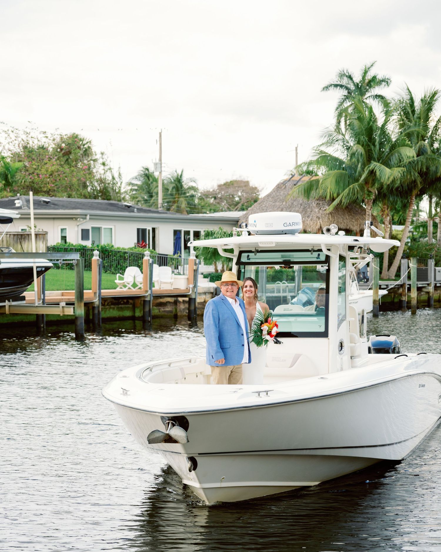 A series of white center console fishing boats cruising through a waterway lined with palm trees and docks.