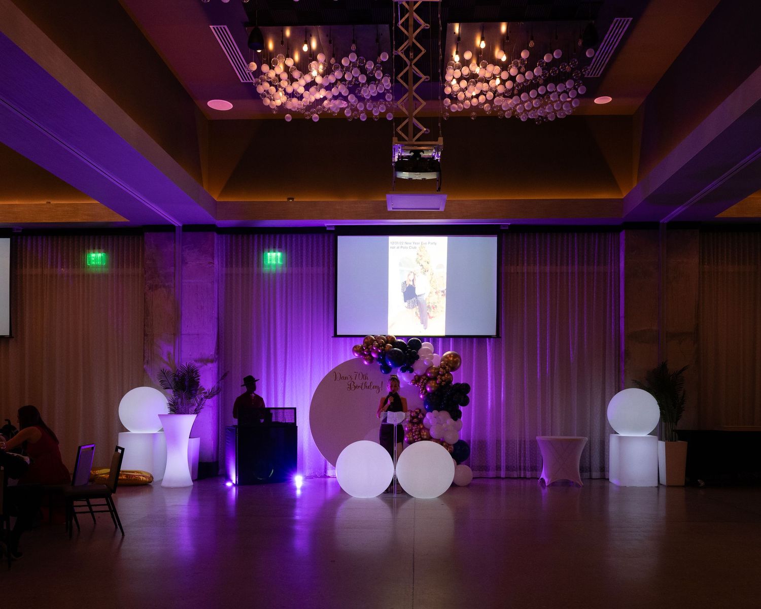 Purple uplighting illuminates an empty ballroom with white glowing orbs and dance floor.