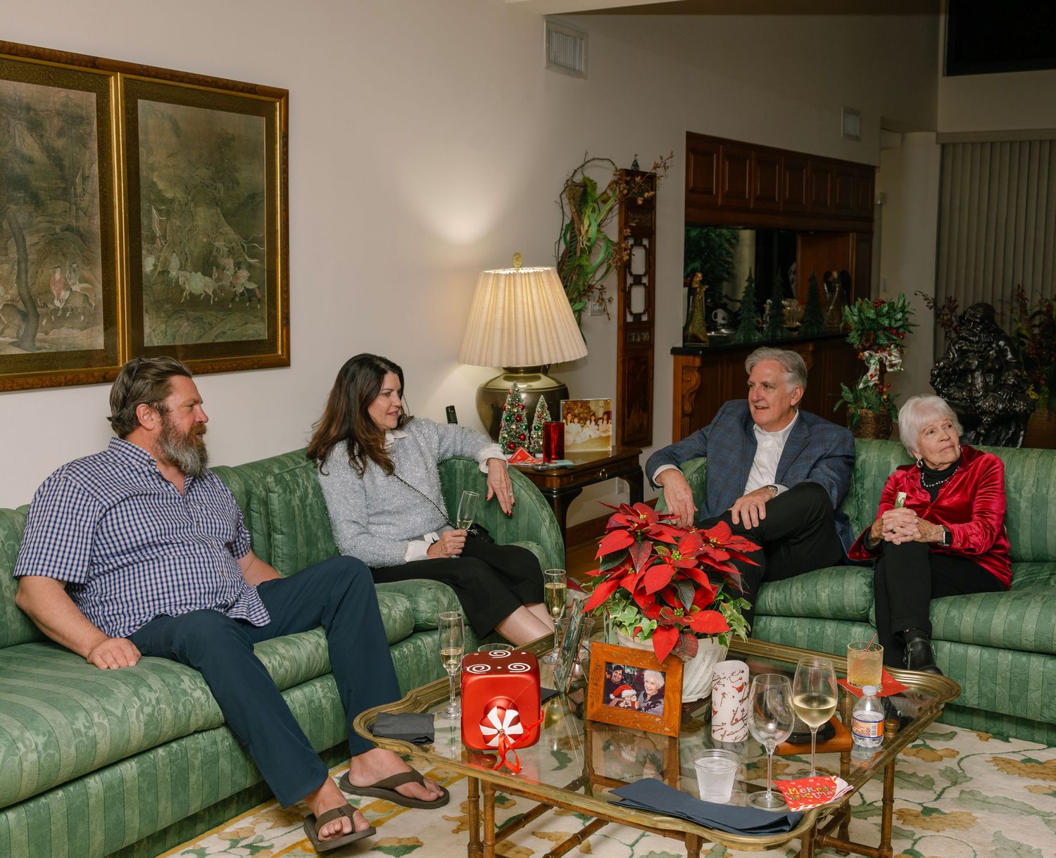 Family gathering in a living room with green couches and holiday decorations on the coffee table.