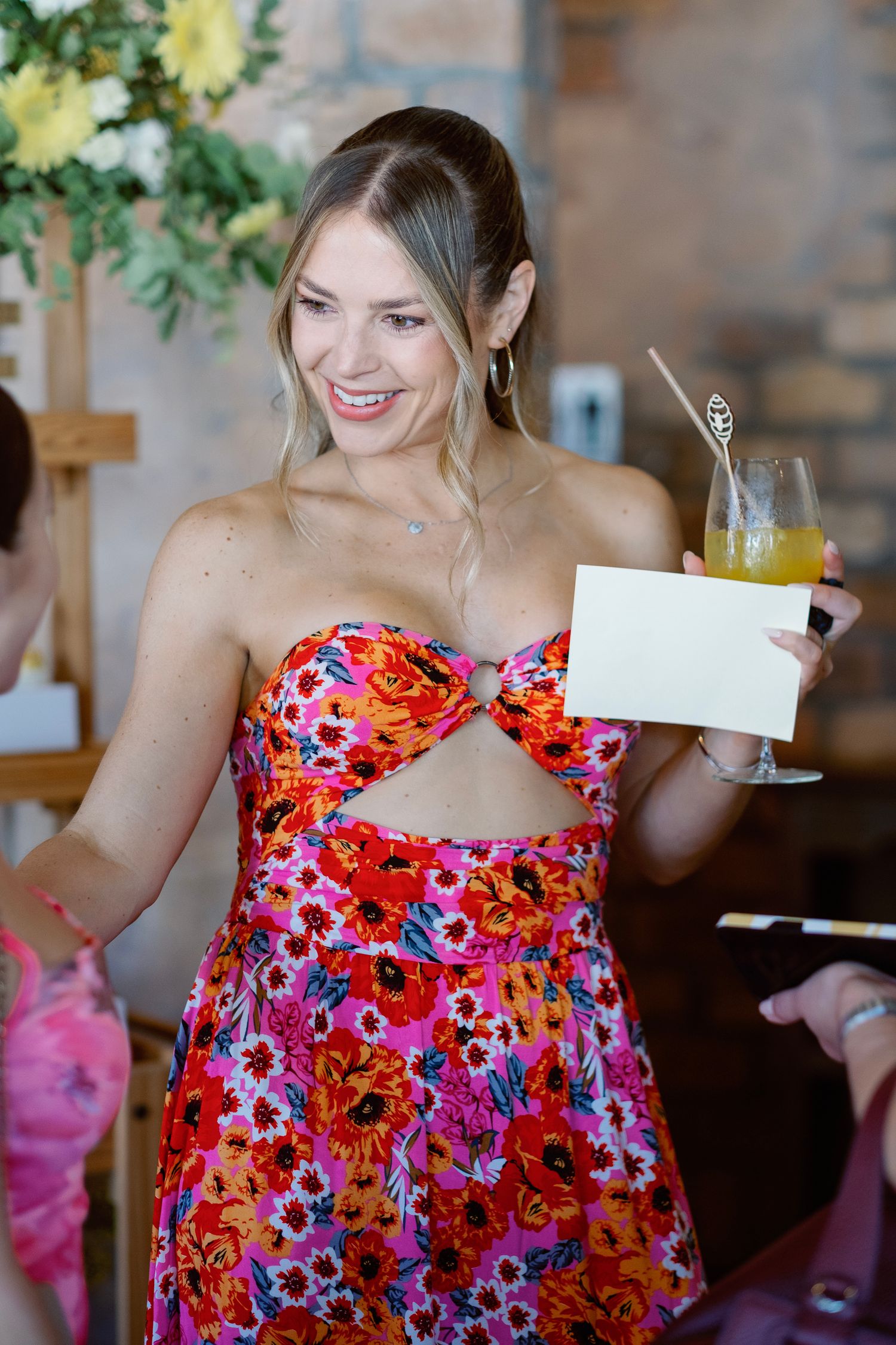 A vibrant floral dress is worn at a festive indoor celebration with drinks and decor.