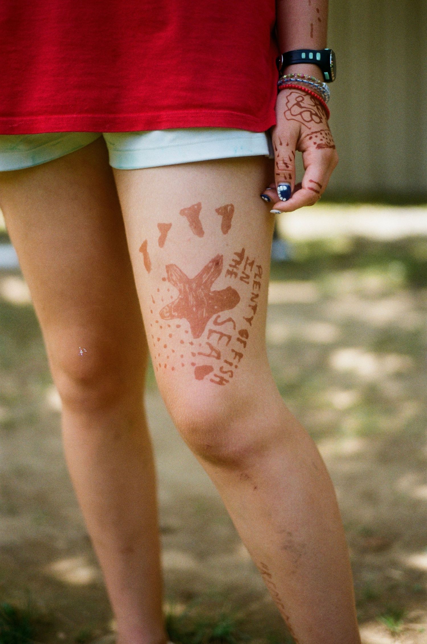 Close-up of a leg with a henna tattoo featuring a starfish and sea-themed design, worn by a person in a red dress.