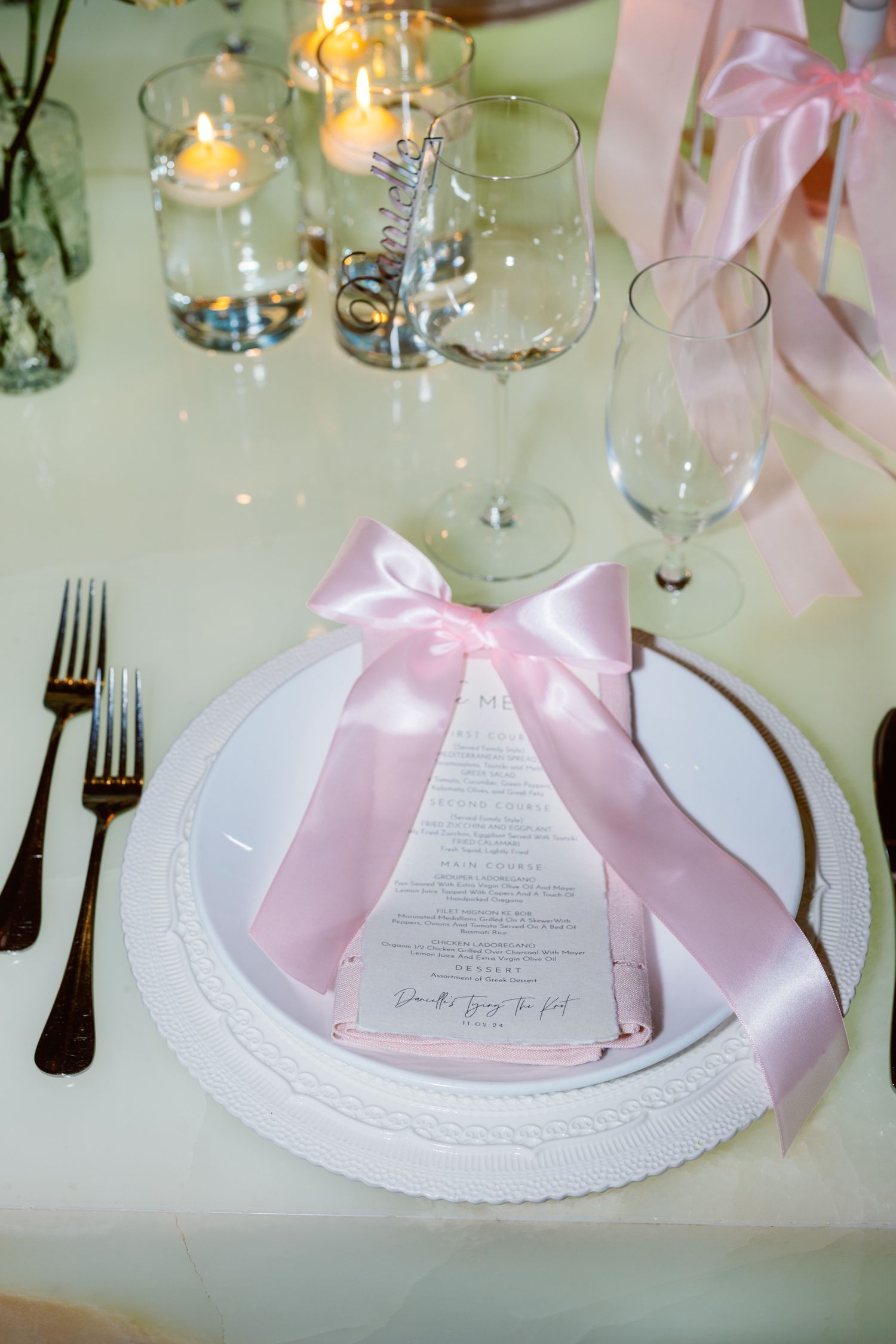 Elegant wedding table settings with pink ribbon bows and menu cards on white plates at a formal reception.