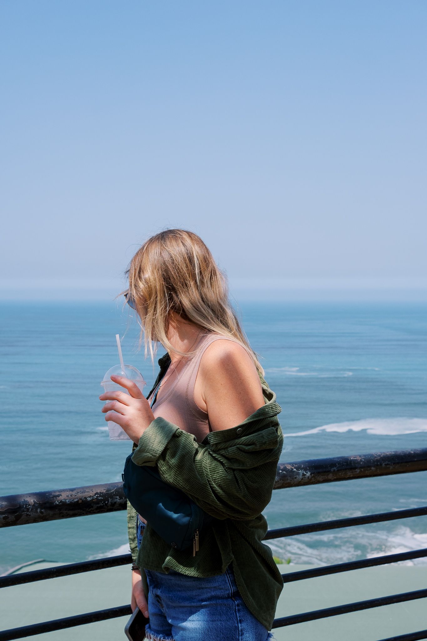 Person taking photos at an oceanside railing on a bright sunny day.