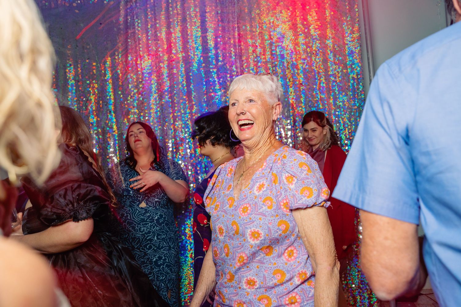 Wedding reception guests dancing under colorful disco lights and sparkly backdrop.