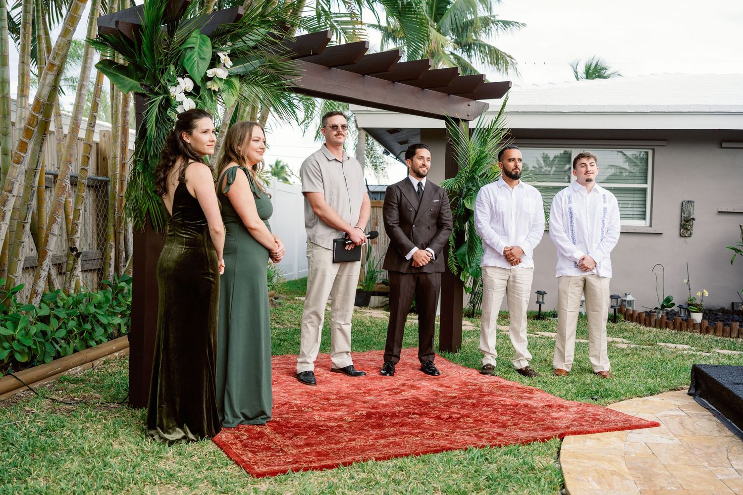 A small outdoor wedding ceremony setup with a red carpet and palm trees in the background.