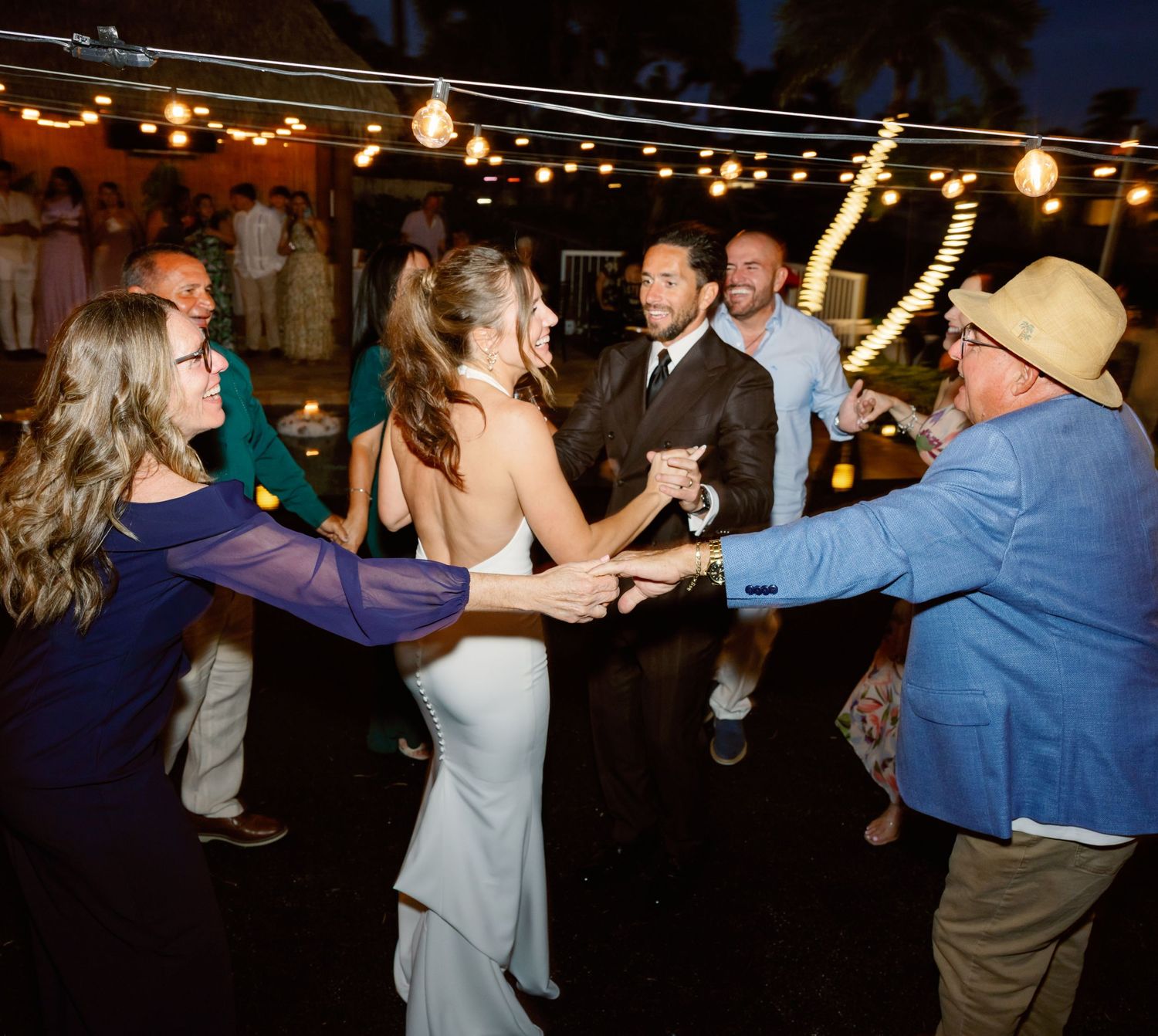 Wedding reception dance floor with guests dancing under string lights at night.