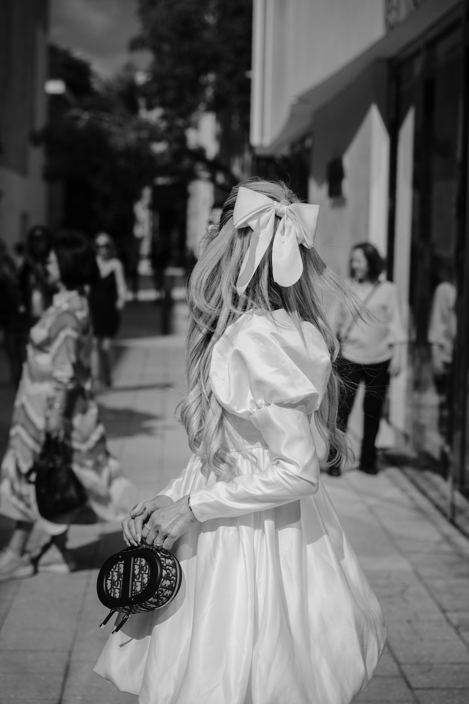 A street performer in a flowing white dress and mask performs an expressive dance routine in an outdoor plaza.