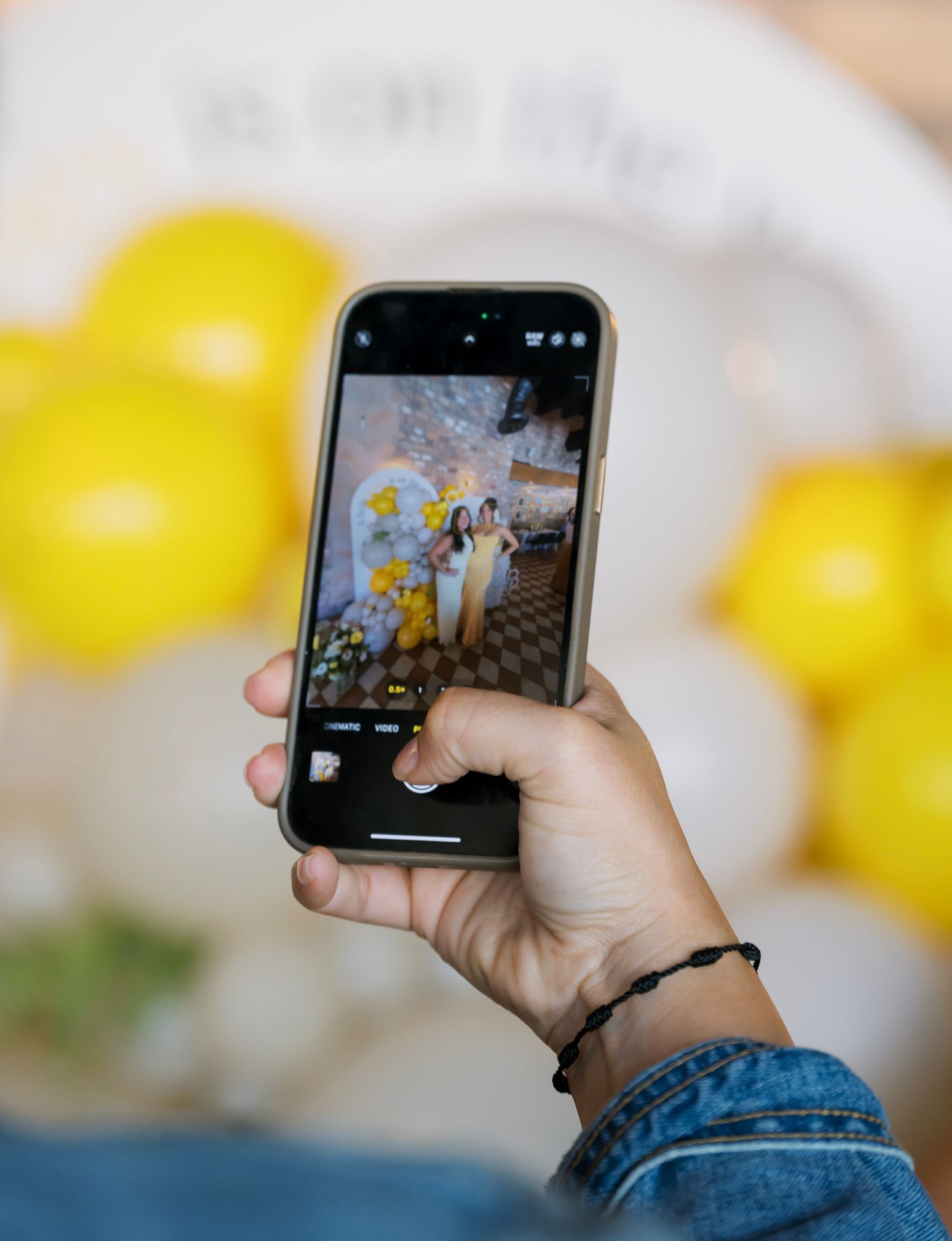 Hand holding a smartphone displaying a colorful game interface with yellow balloons in the background.