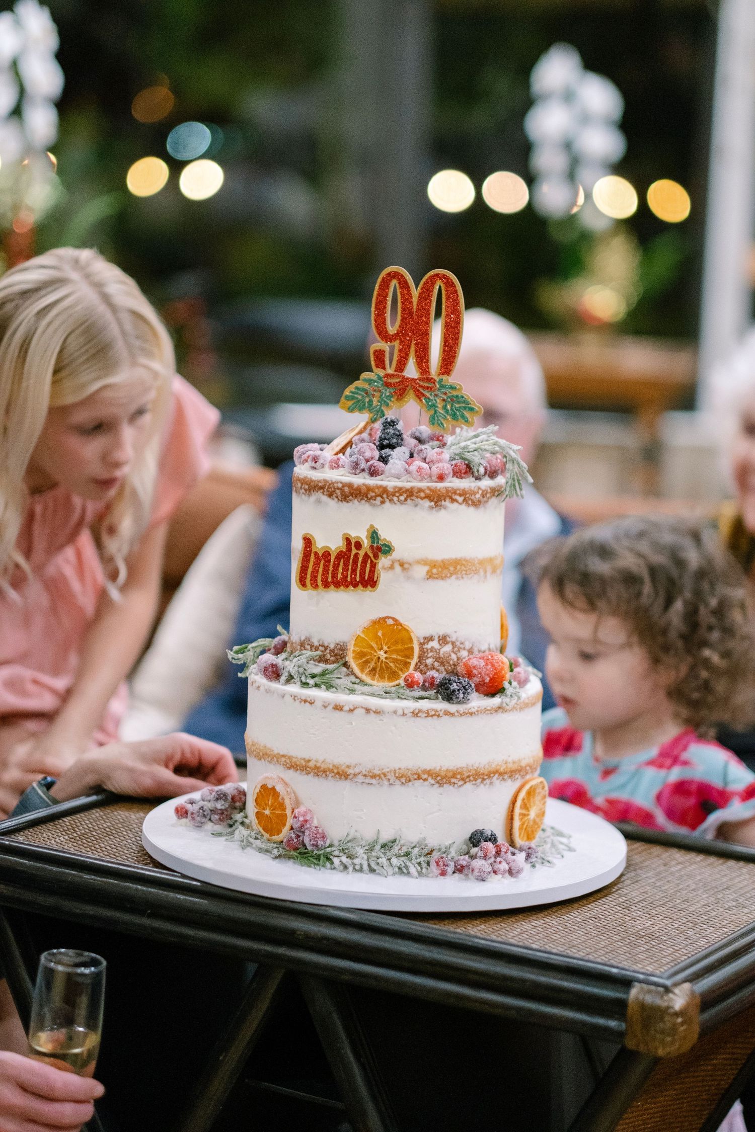 Beautiful semi-naked cake decorated with dried oranges and a gold number 90 topper for milestone celebration.