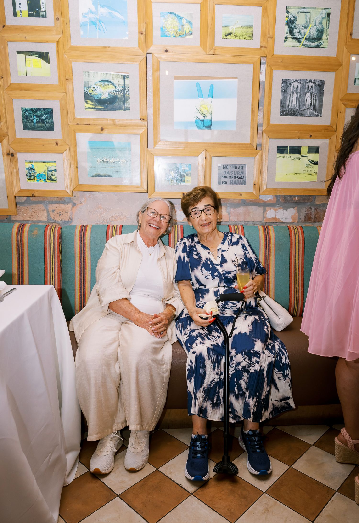 People wearing coordinating blue and white floral outfits sit together in a room with framed artwork on the walls.