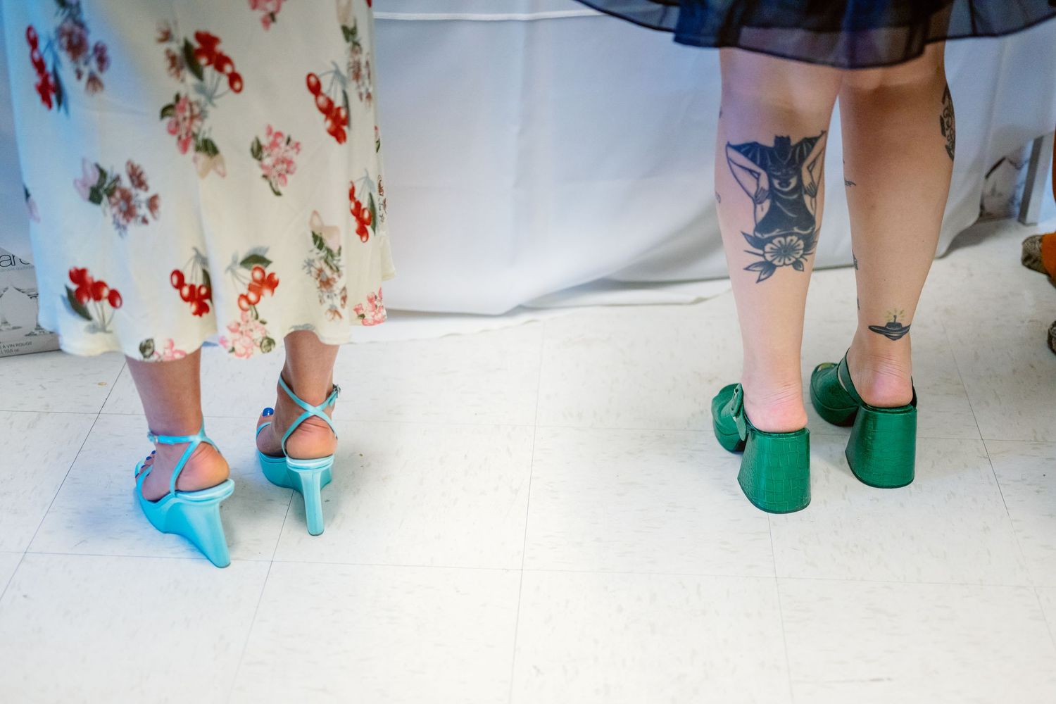 Multiple pairs of feet wearing colorful socks and shoes stand against a white floor with floral decor visible.
