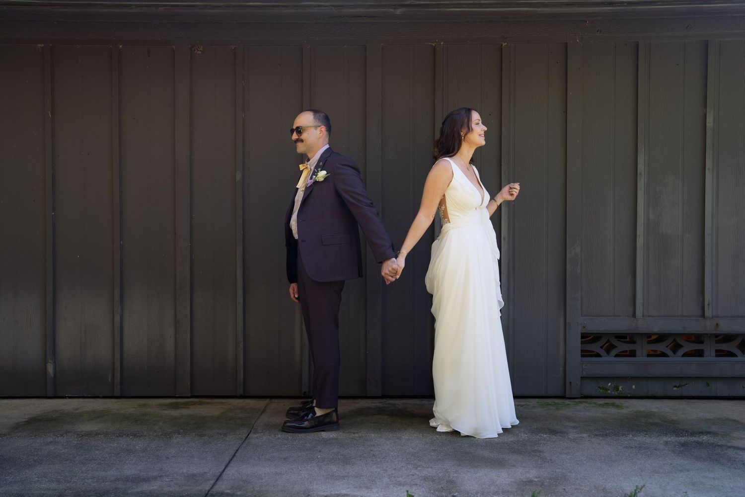 A bride and groom walk along a covered walkway while holding hands on their wedding day.