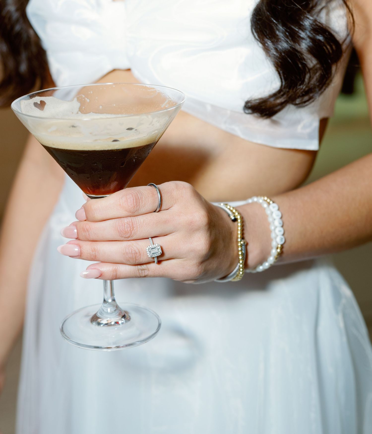 Three hands holding elegant cocktail glasses filled with creamy drinks against a light background.