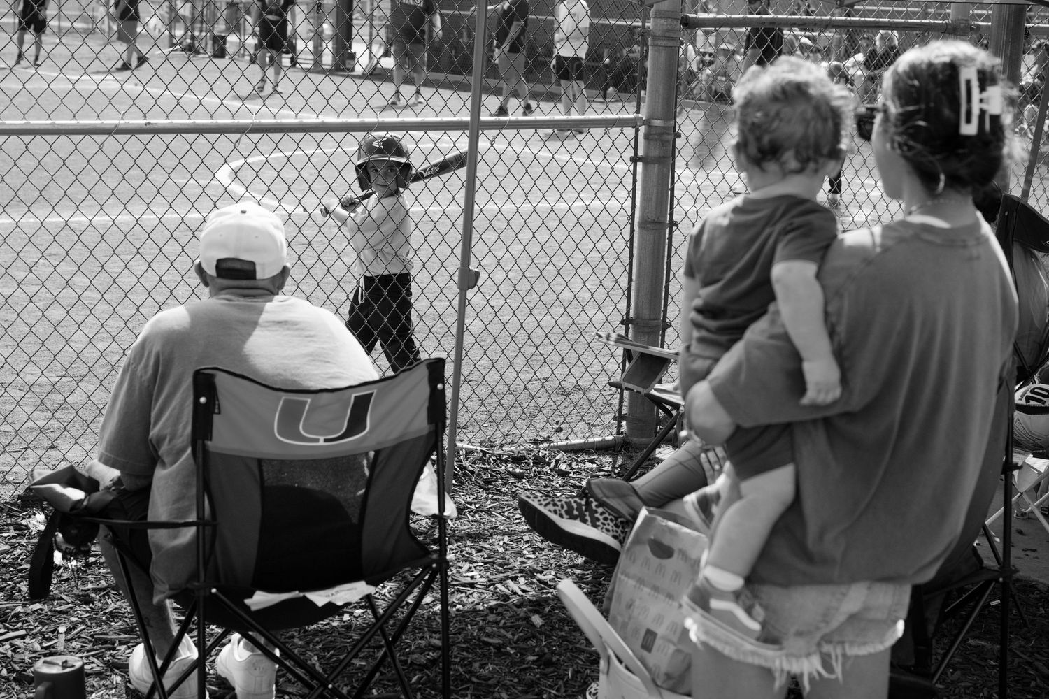 Spectators watch a youth baseball game through a chain-link fence.