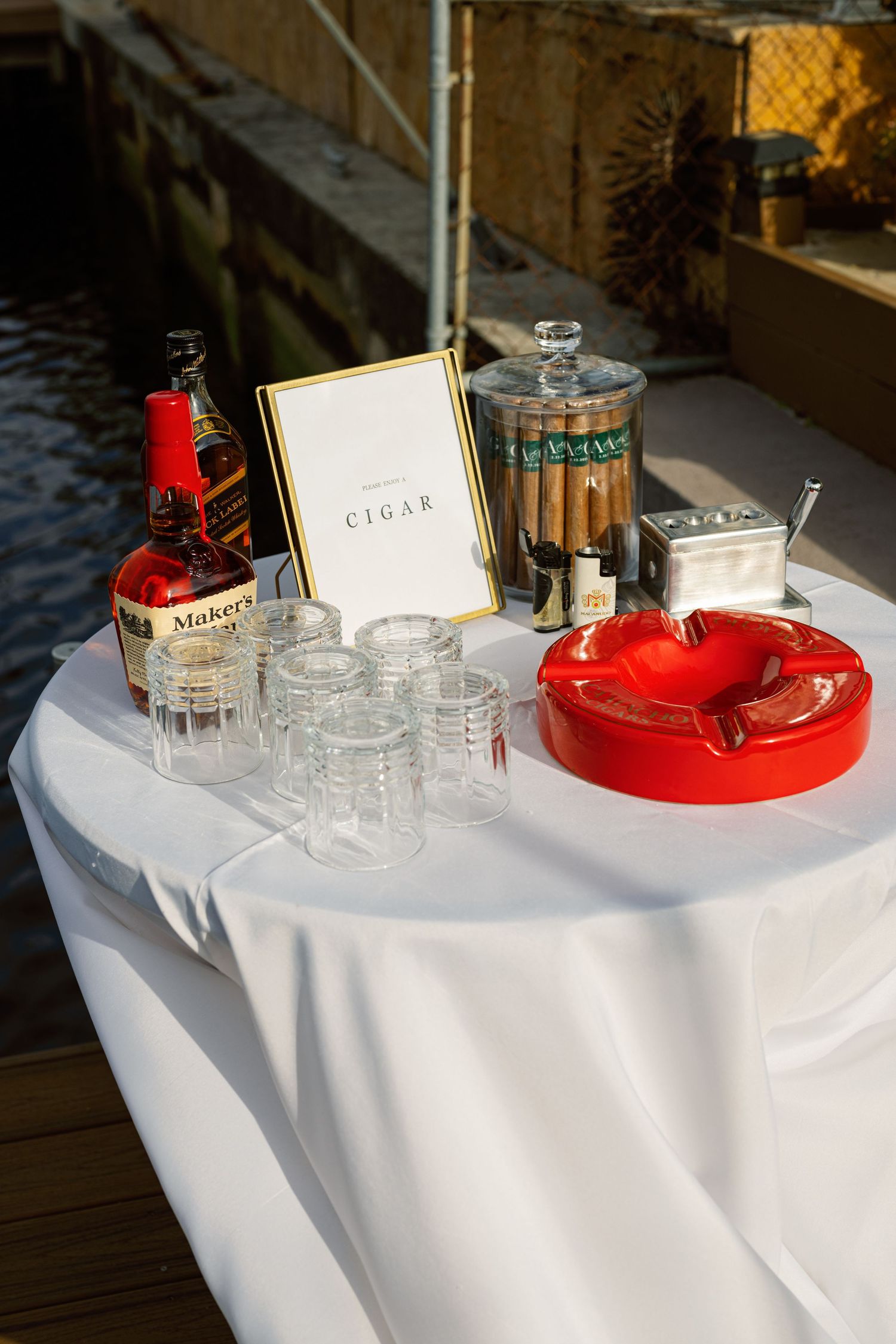 Elegant cigar and drinks station with white tablecloth and red serving trays at an event.