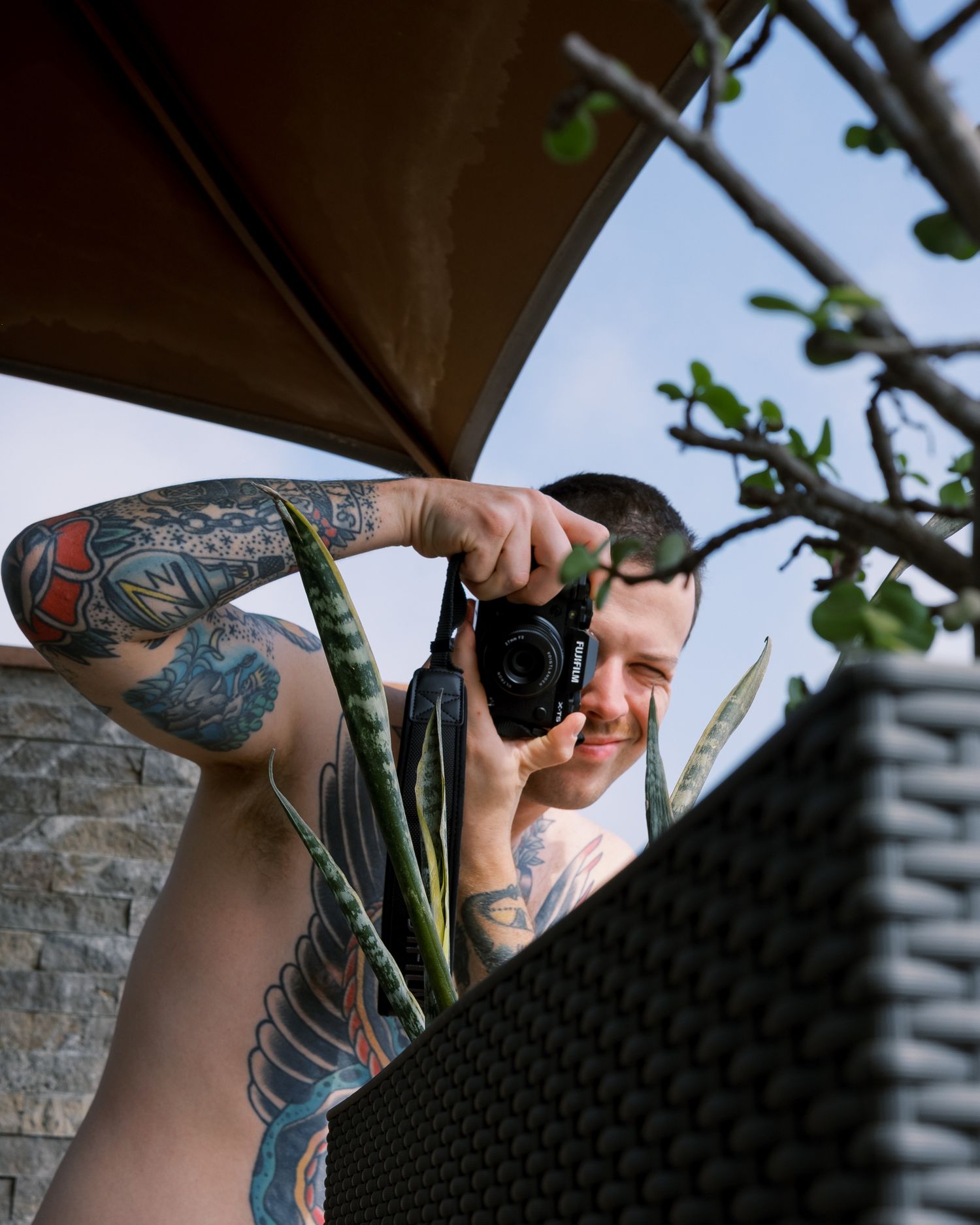 A person with tattoos aims a power drill upward while installing something on a ceiling or overhead structure.