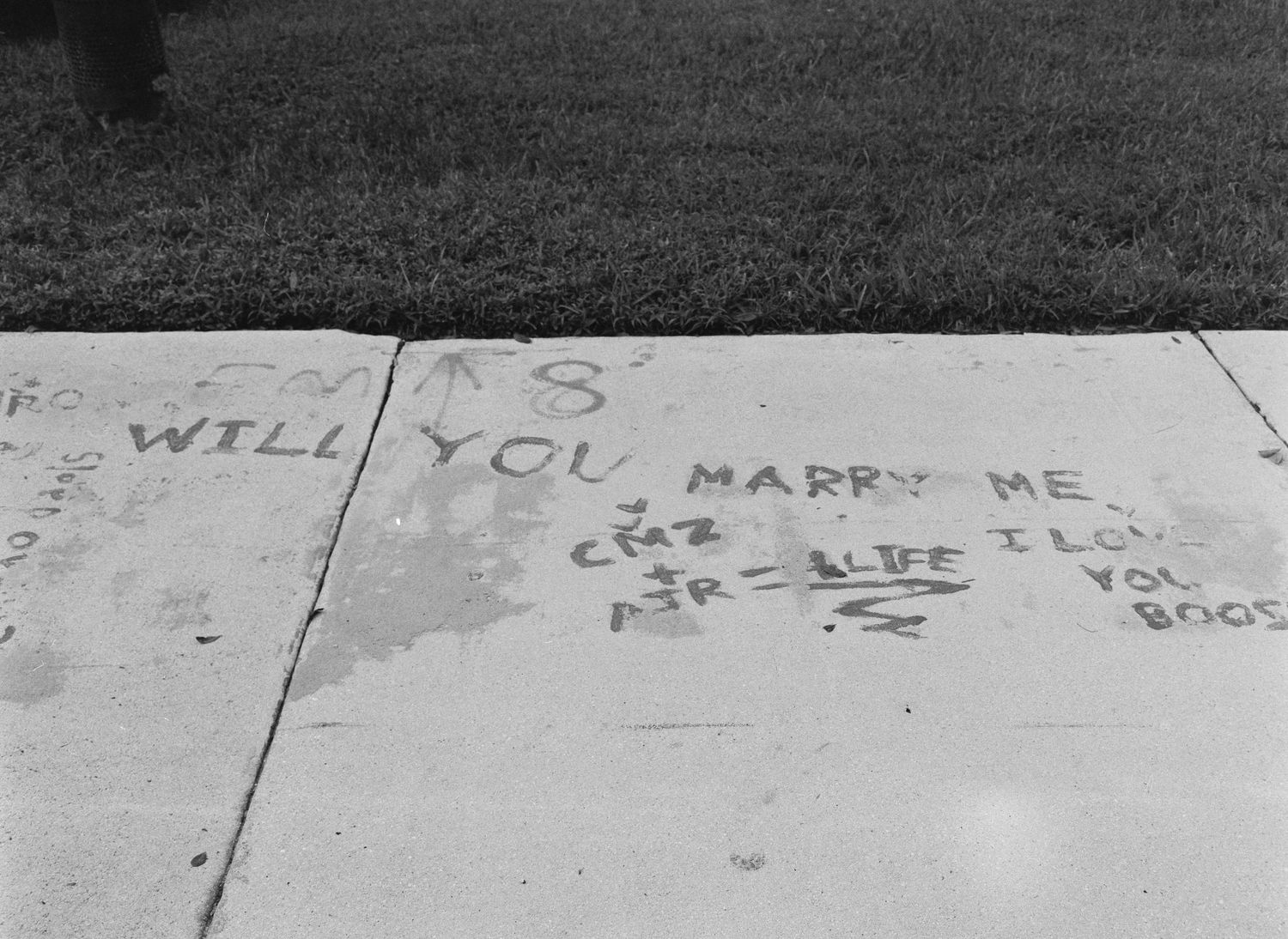 Black and white photo of a sidewalk marriage proposal written in chalk reading Will You Marry Me.