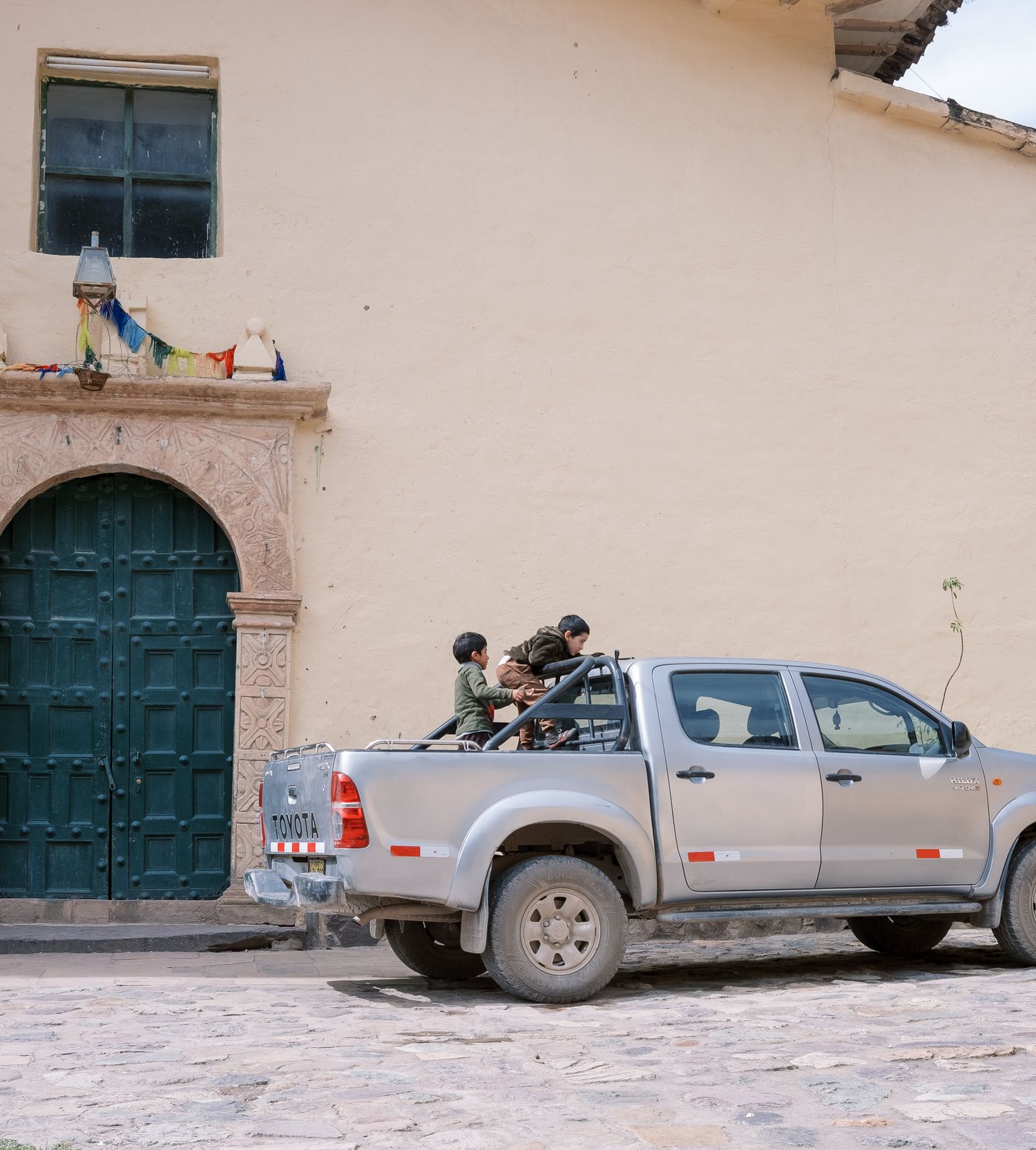 Silver Toyota pickup truck parked on cobblestone street near historic building with teal door in Peru.