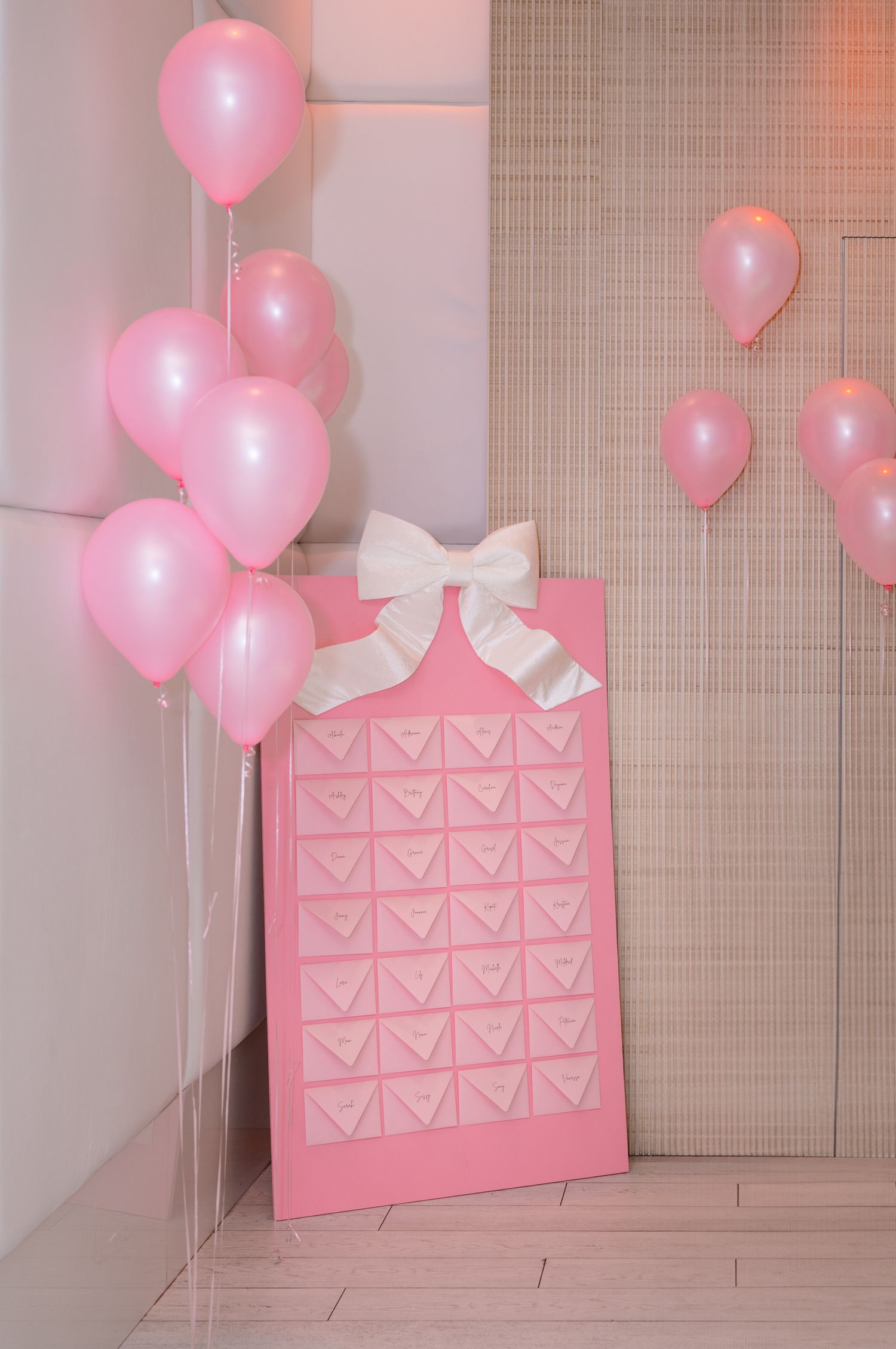 Pink heart-shaped envelopes with white bows arranged on wall with floating pink balloons creating a romantic backdrop.