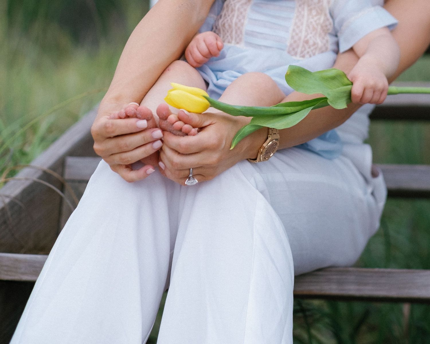 Close up details of hands holding colorful tulips against a white dress in a garden setting.