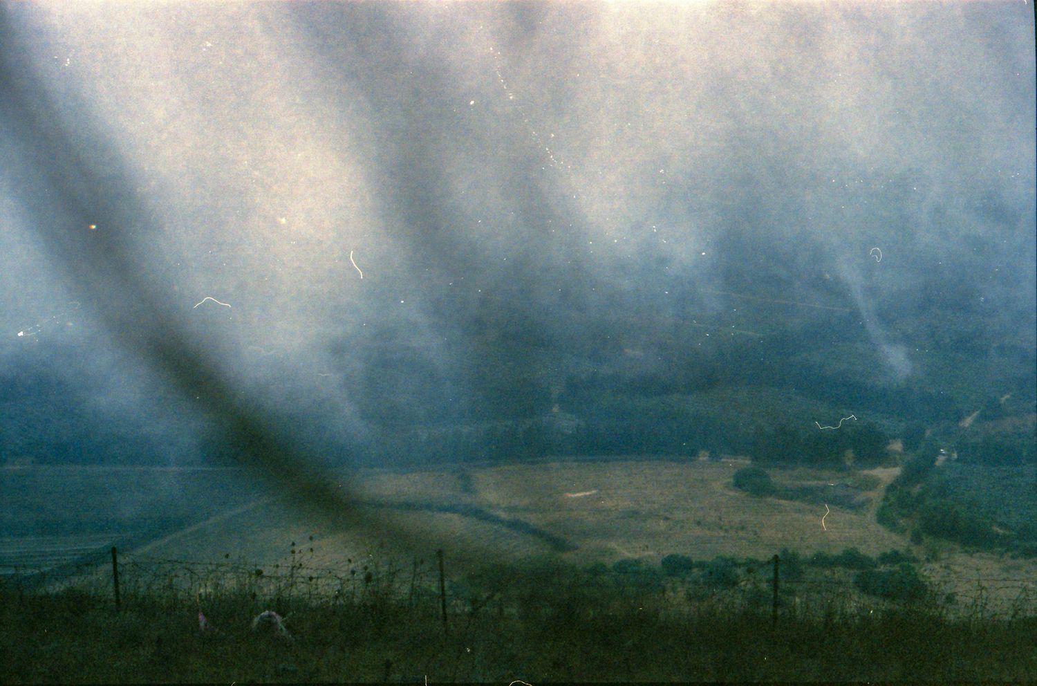 Aerial view of a misty rural valley with green fields, a winding road, and atmospheric light rays on a cloudy day.