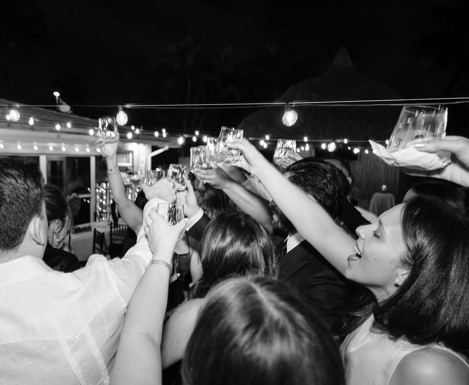 Crowd of concert-goers raise their hands in unison during a dark nighttime performance.