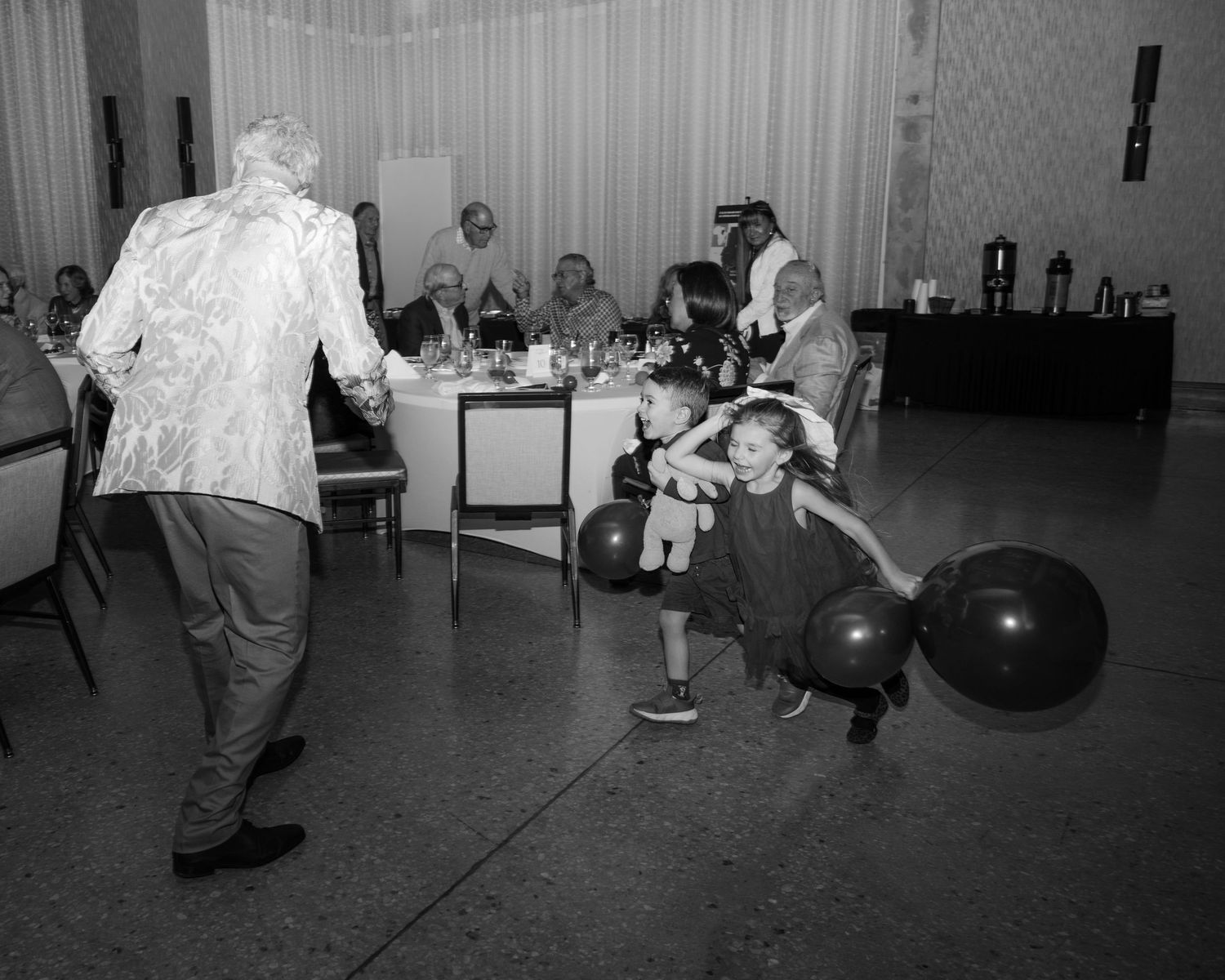 Black and white photo of people dancing at a social gathering in a large indoor space.
