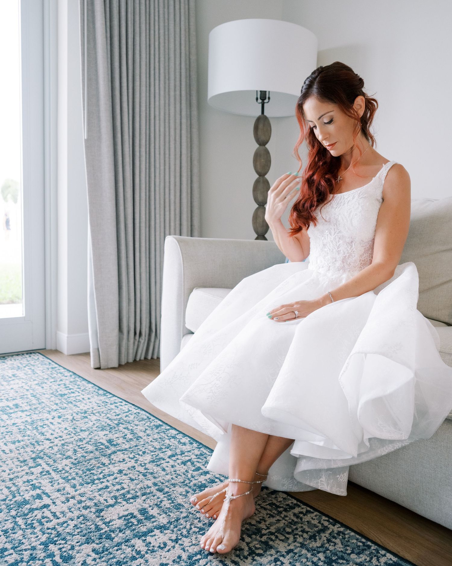 A bride in a white wedding dress sits elegantly on a patterned blue and white rug in a bright modern room.