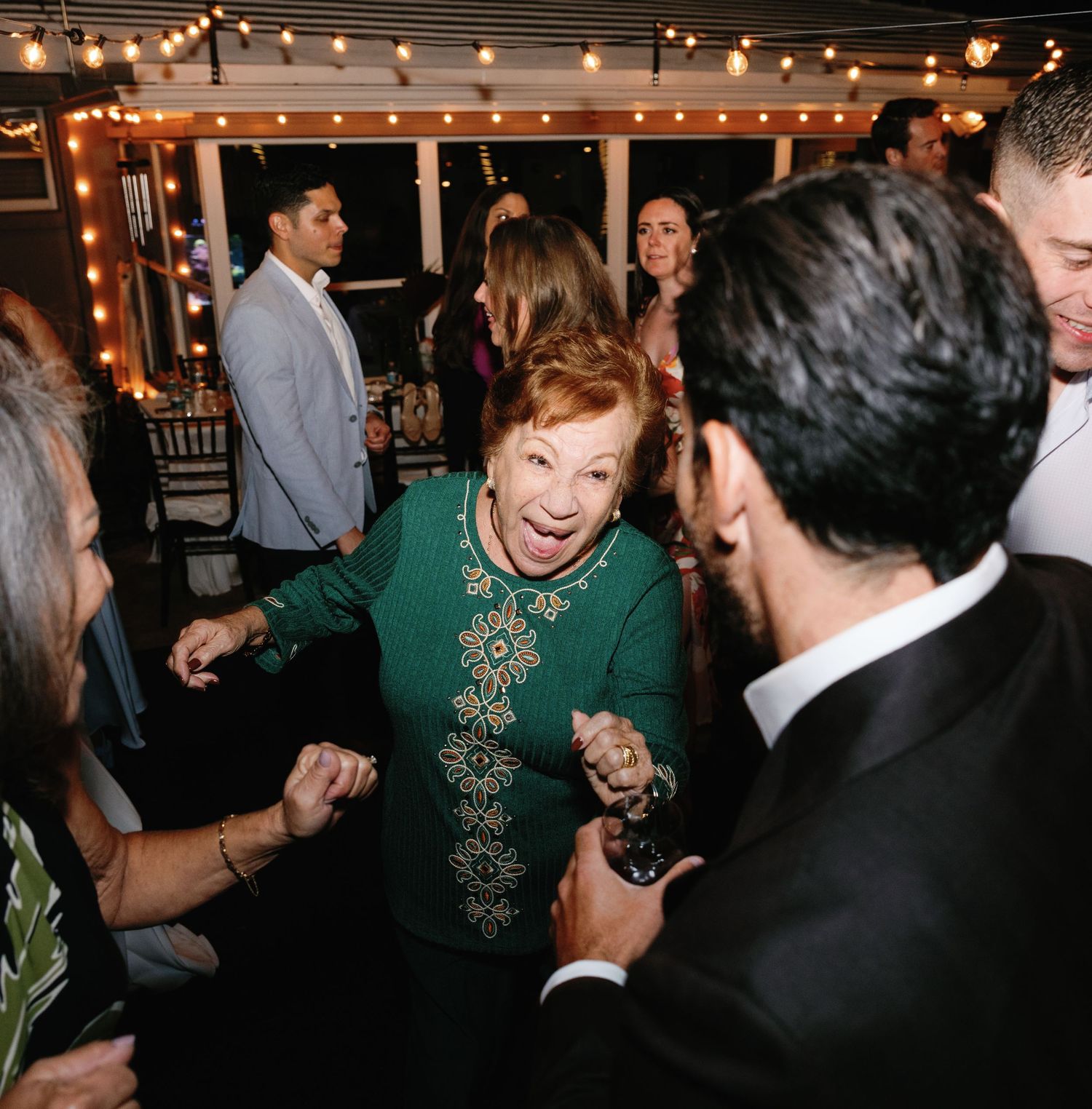 Party guests dance and celebrate under warm string lights at an indoor evening celebration.