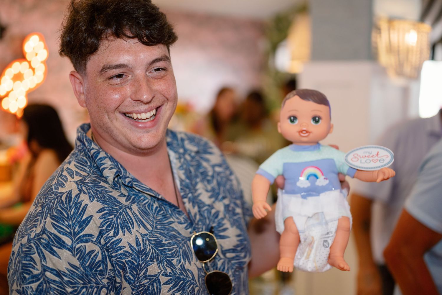 A group of people at a party hold up baby-themed decorations and toys in celebration.