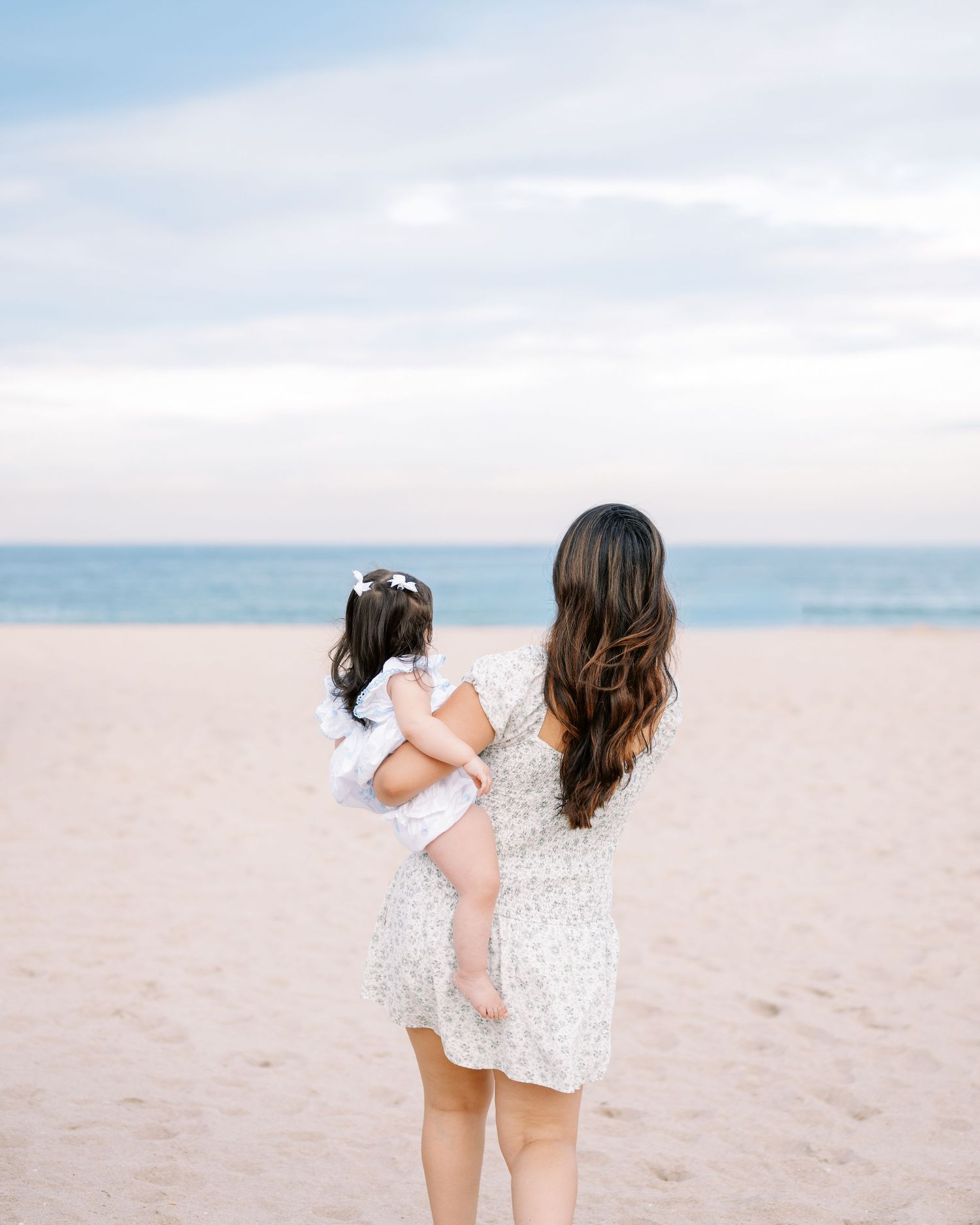 Parent and child playing together on a sandy beach in coordinated outfits.