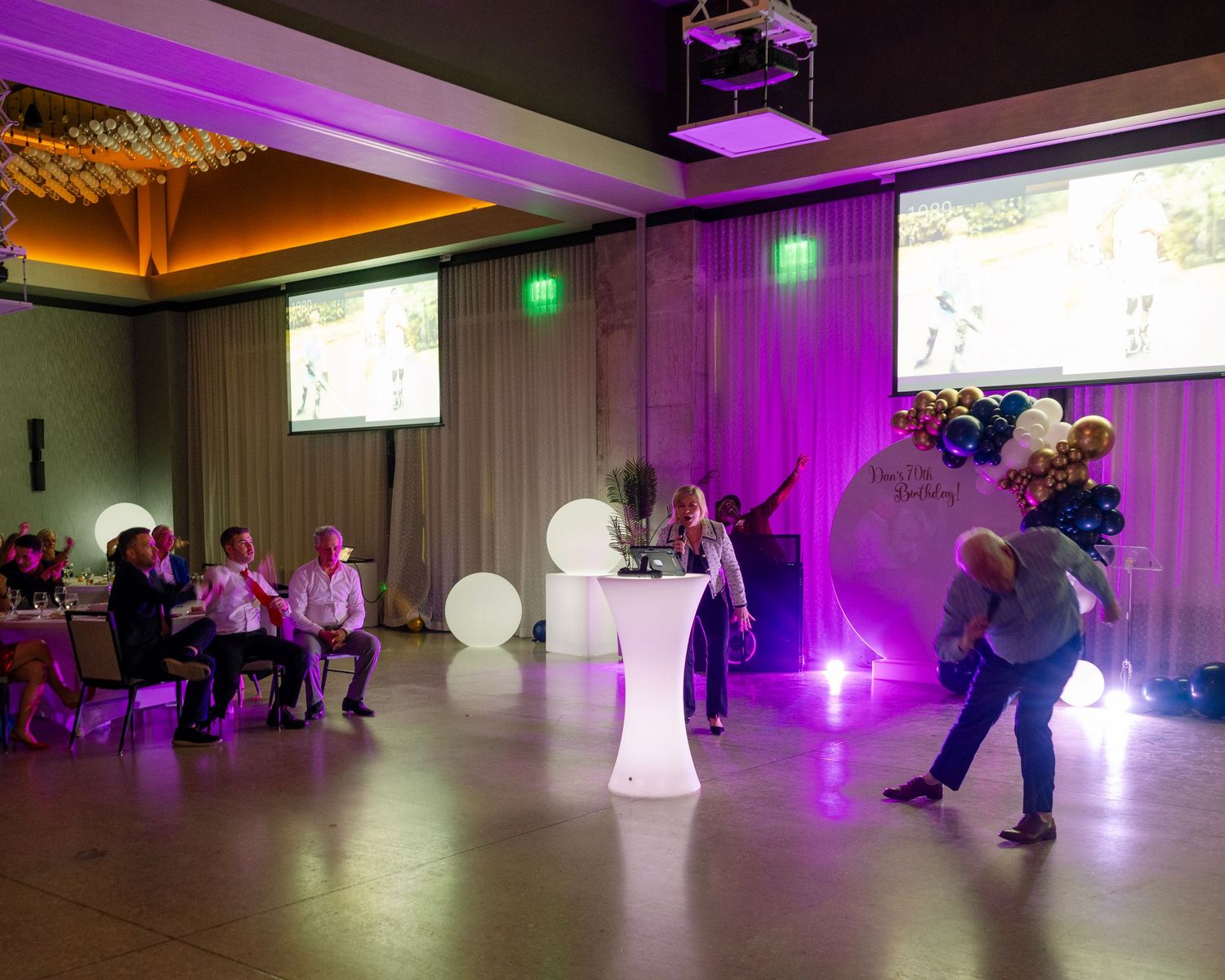 Ballroom illuminated with purple uplighting as couples dance across the floor.