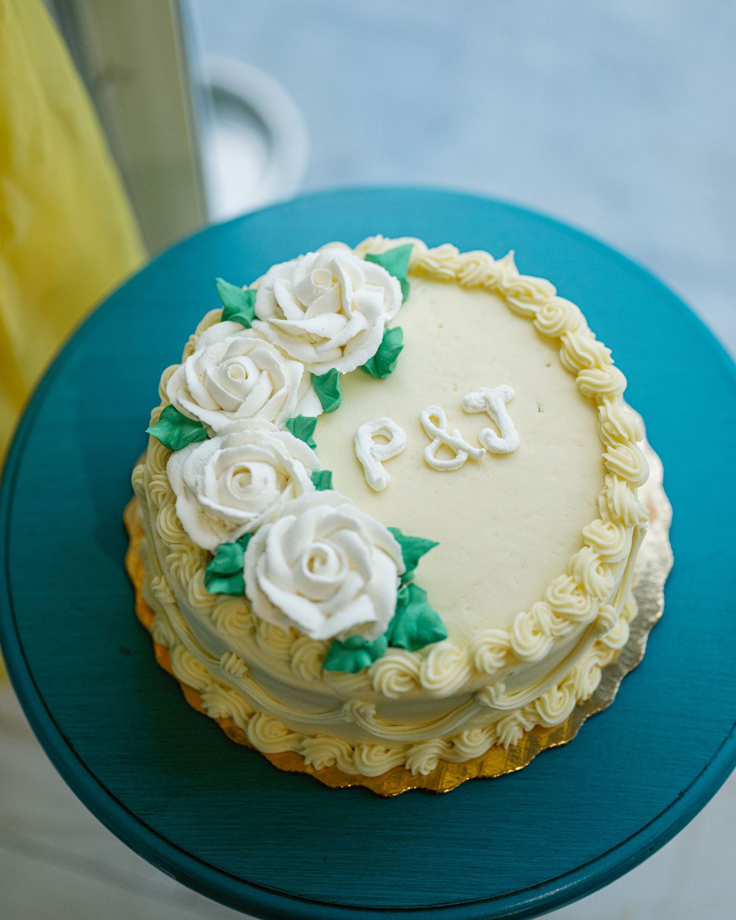 White frosted cake with decorative roses on a turquoise cake stand.
