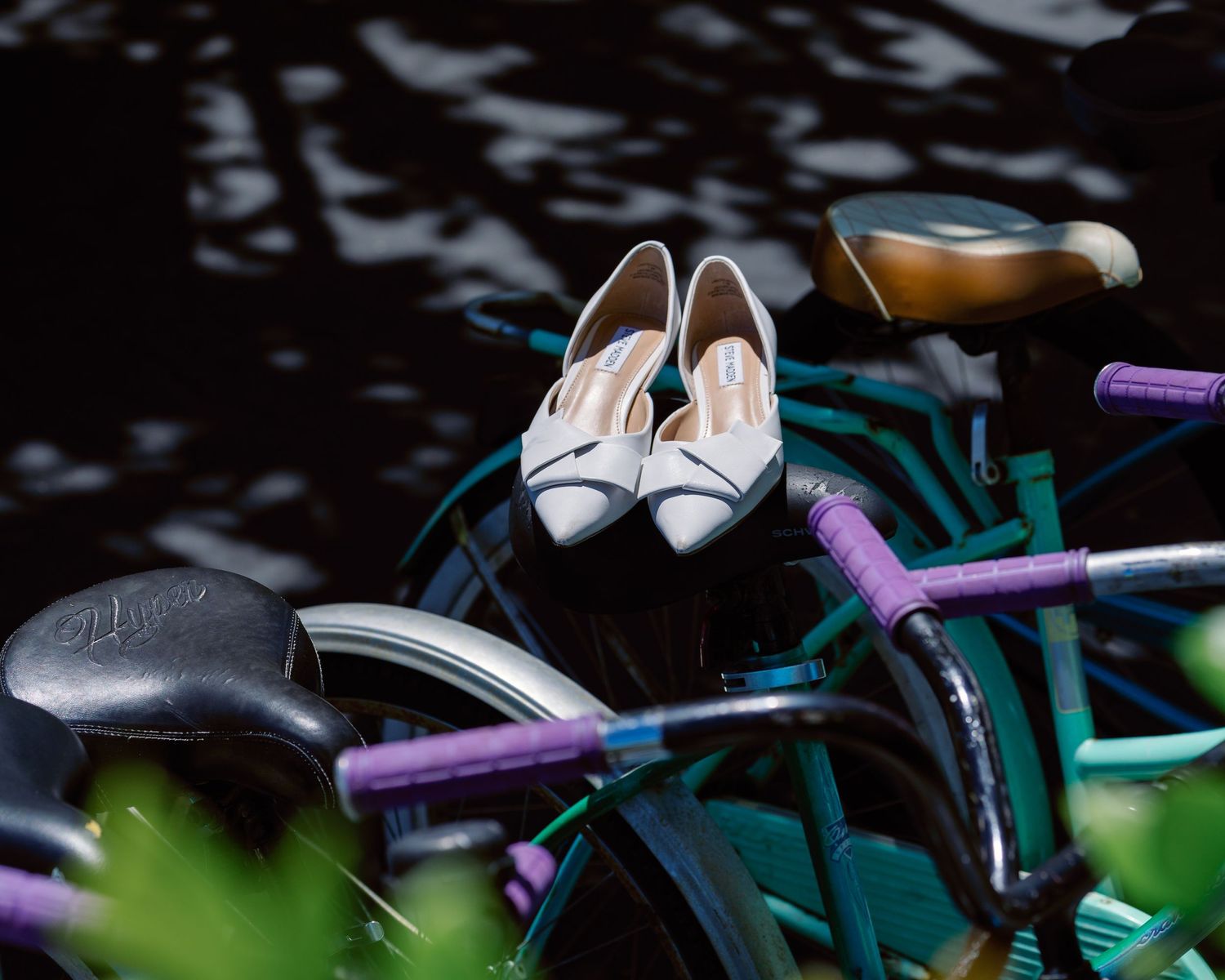A close-up of a turquoise bicycle frame with white shoes and purple accessories against a dark background.