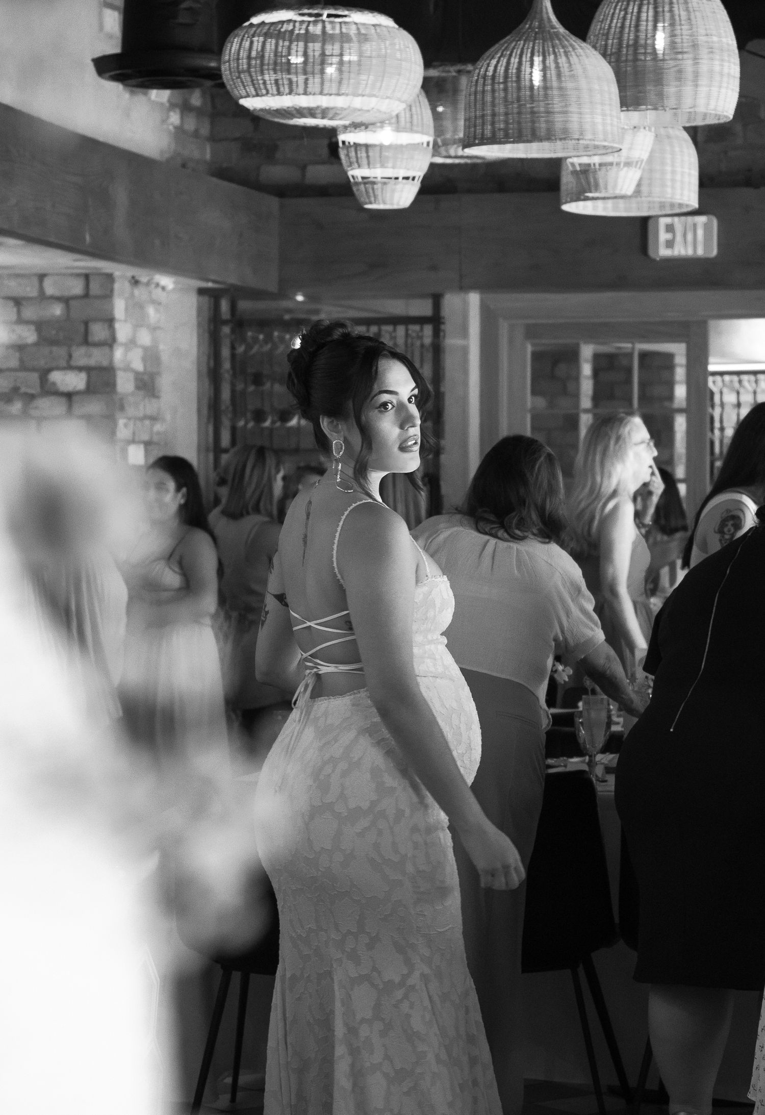 Guests dancing and mingling at an indoor event venue with wicker pendant lights hanging from the ceiling.