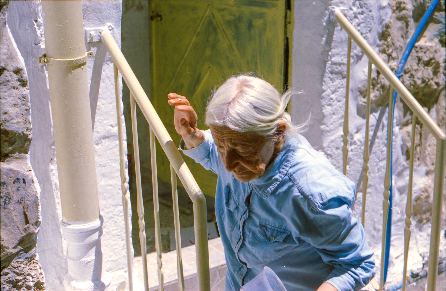 Someone in a light blue jacket and headscarf climbs white metal stairs outdoors.