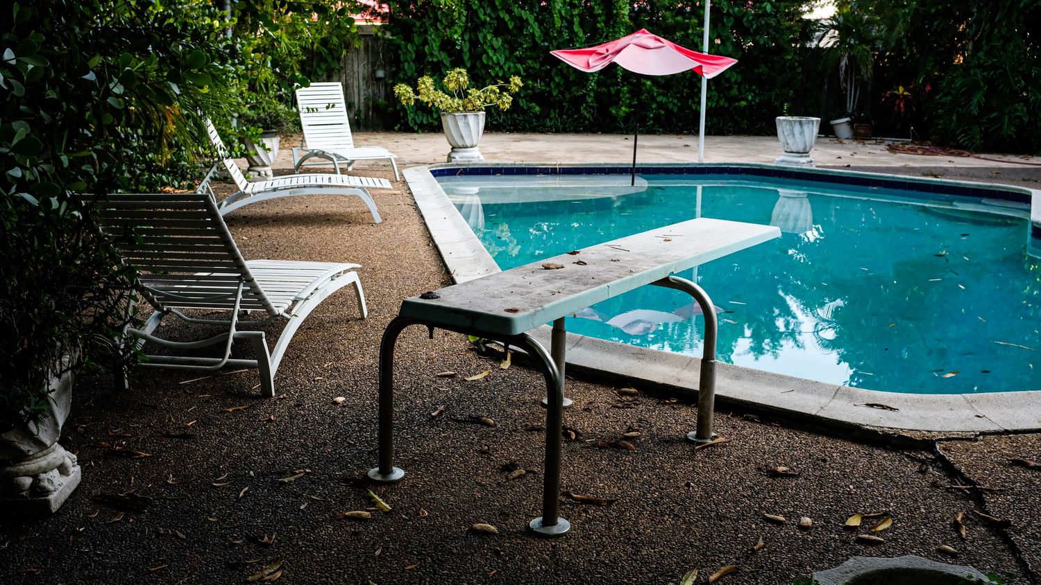 A poolside patio area with red umbrellas and lounge chairs surrounded by lush greenery and trees.