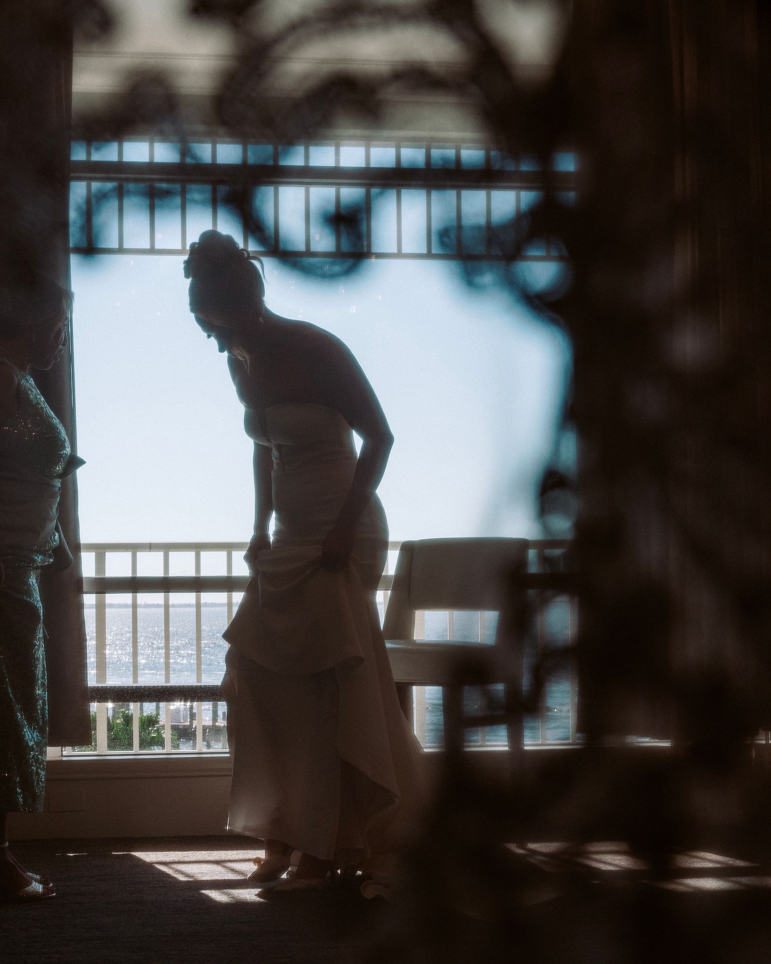 A silhouetted figure sits by a window in a dimly lit room creating a moody atmospheric scene.