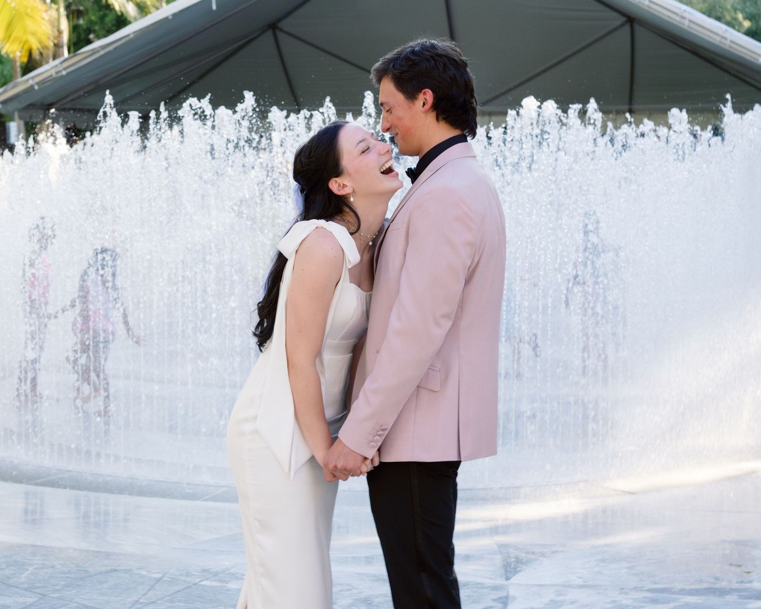 Romantic couple embracing by a fountain in formal attire.