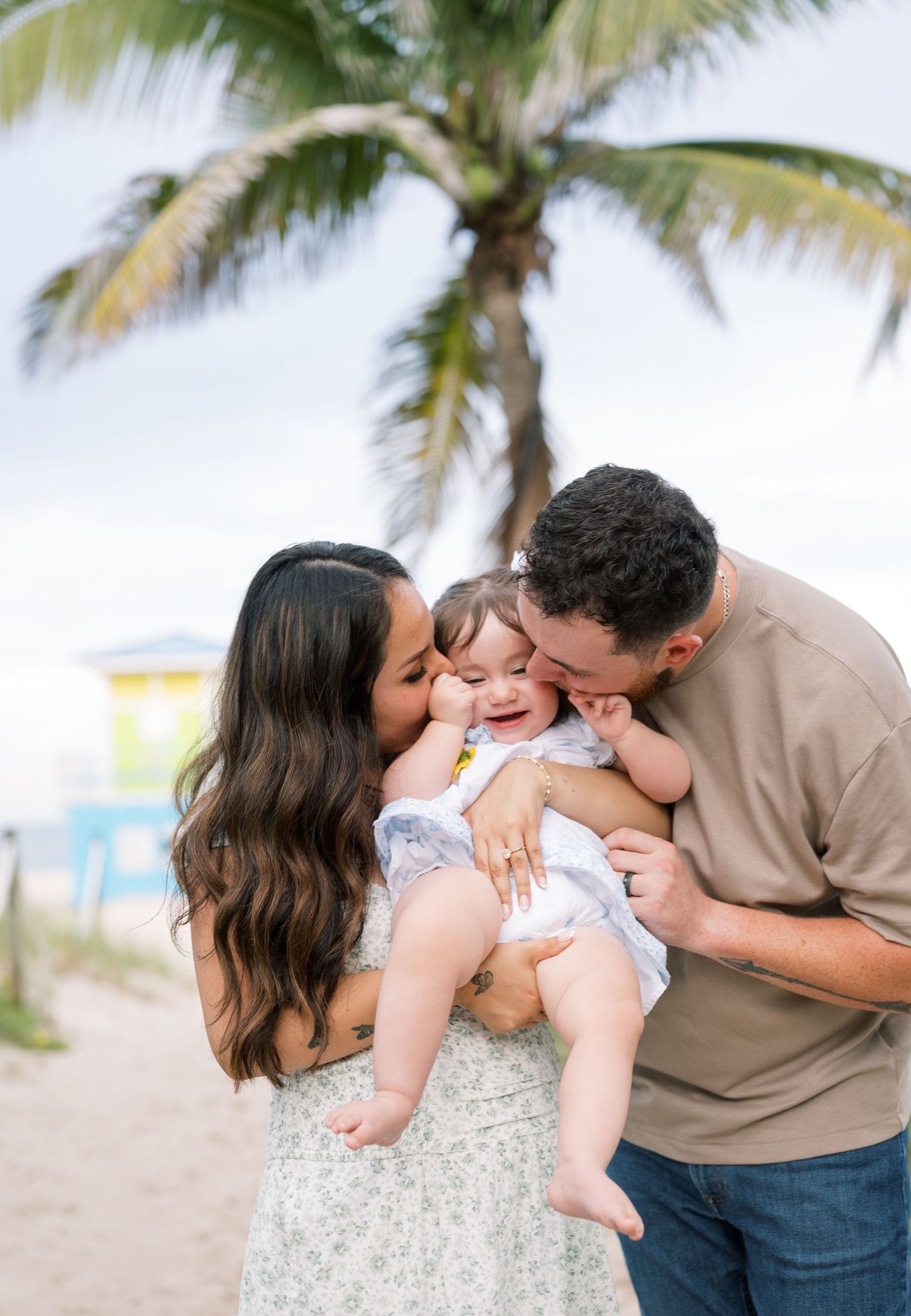 A family shares tender moments together on a beach with palm trees in the background.