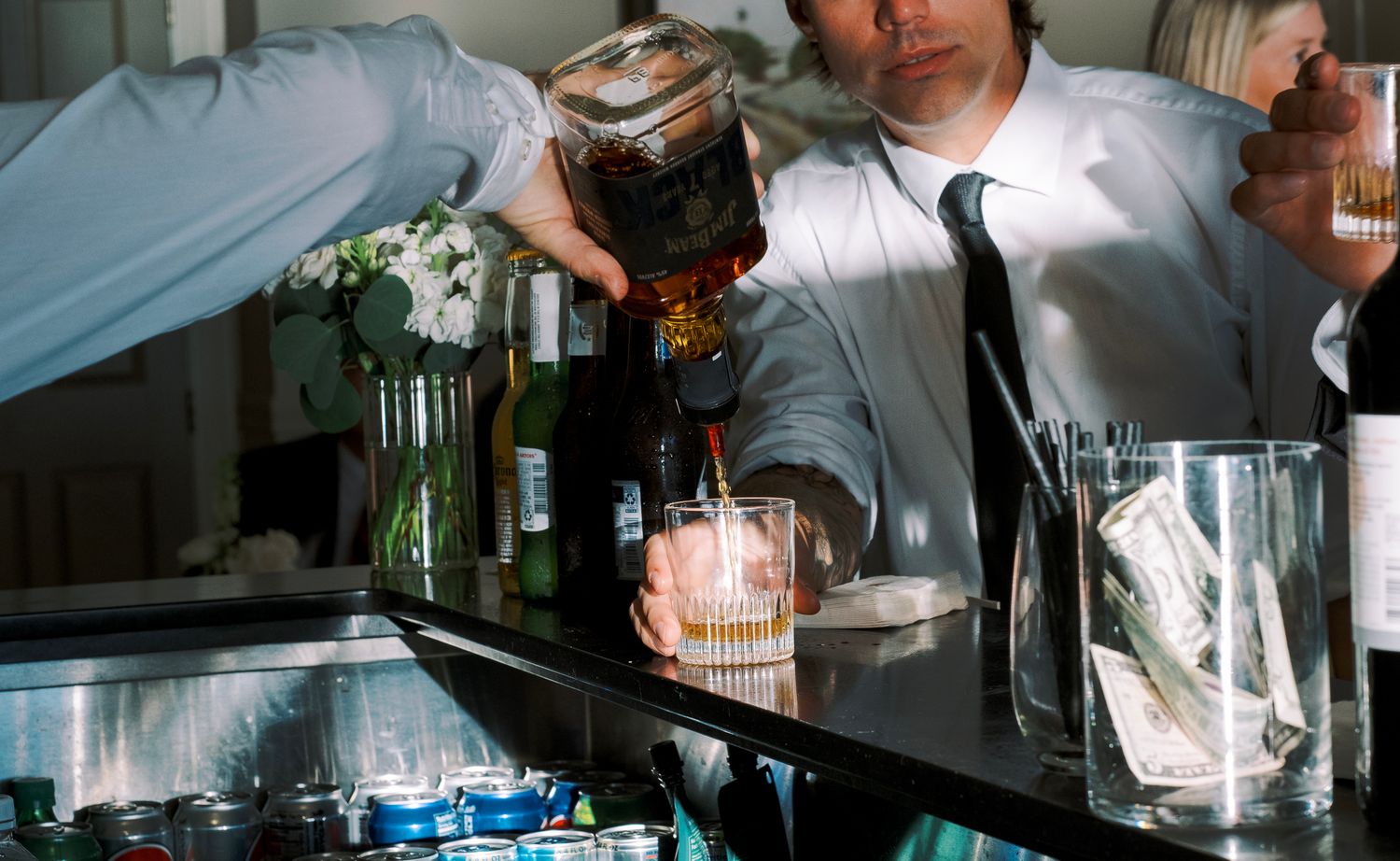 Bartenders prepare cocktails behind a dimly lit bar counter with bottles and glassware visible in the background.