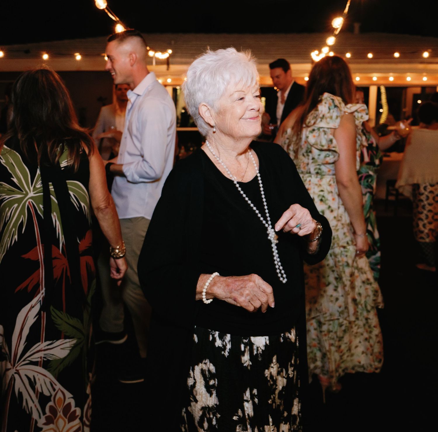 Wedding reception guests dancing and socializing under string lights at night.