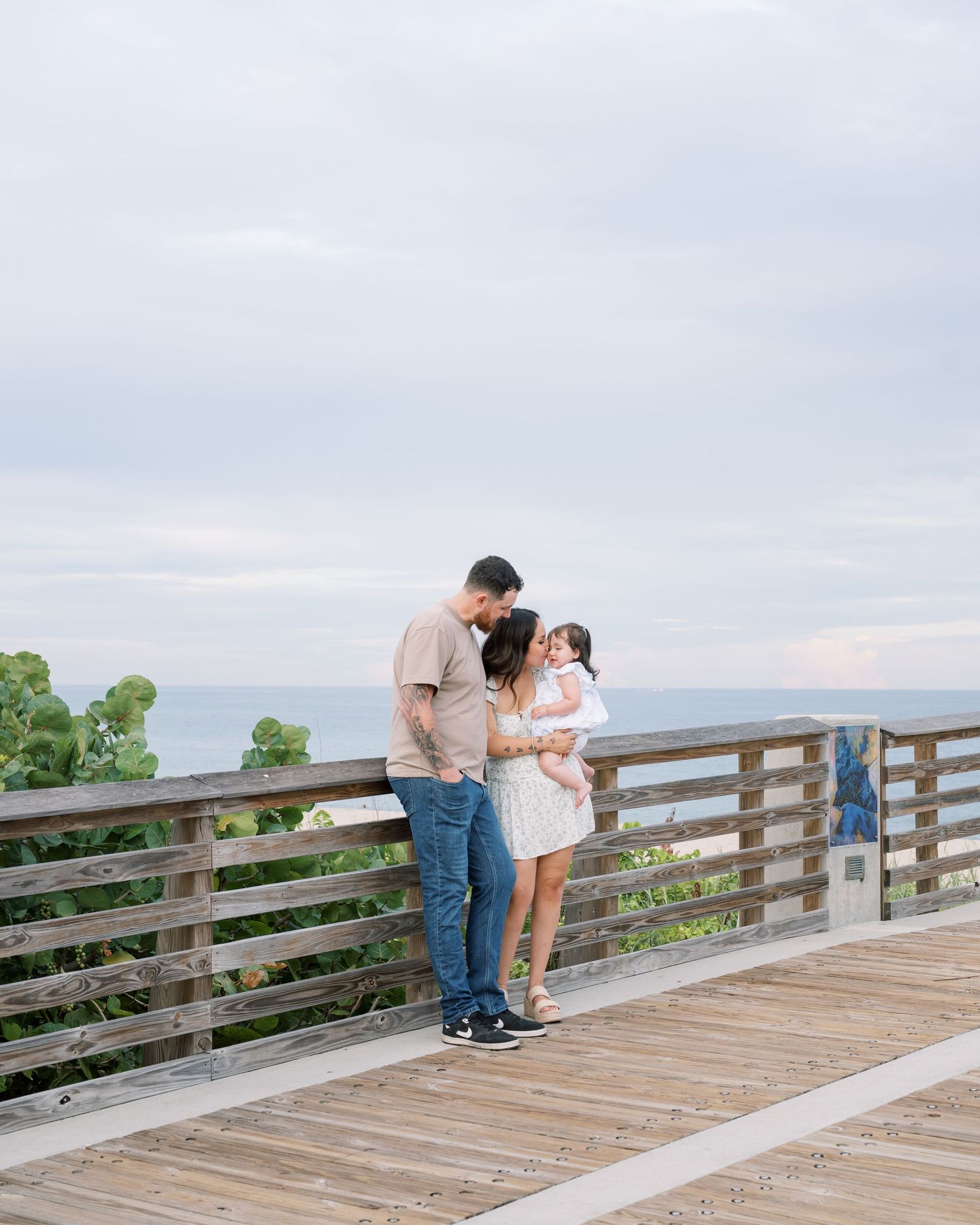 A couple shares a tender moment together on a wooden boardwalk overlooking scenic views on a cloudy day.