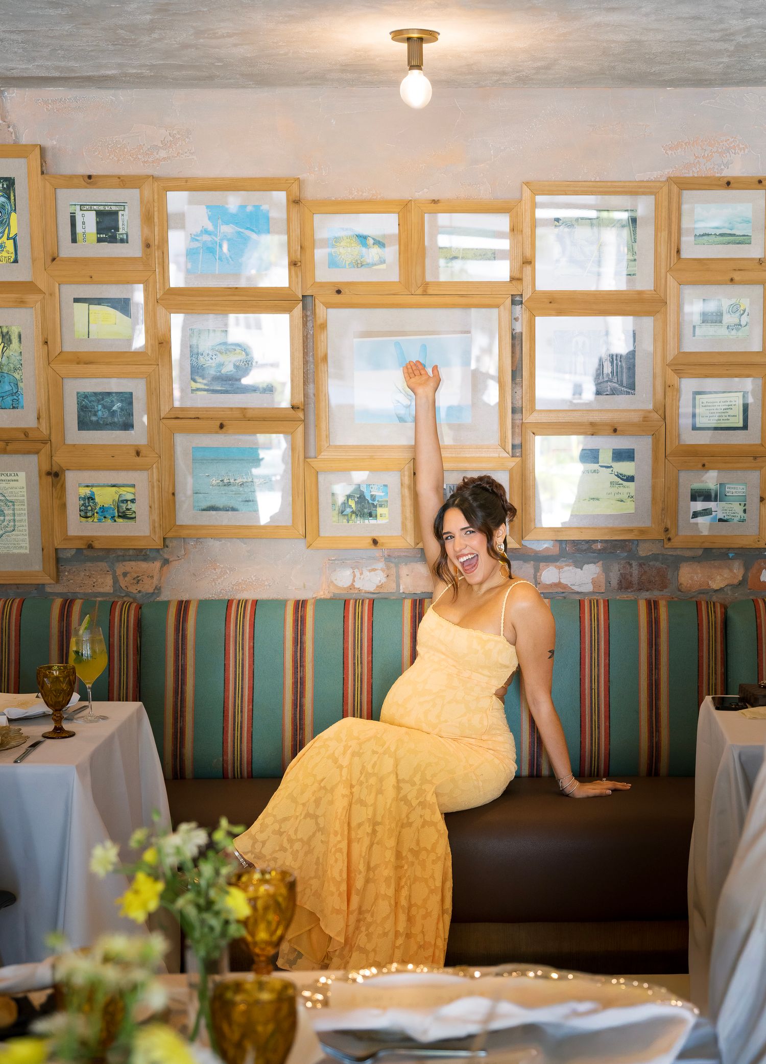 A wedding reception venue with yellow decor, framed artwork on wood-paneled walls, and floral centerpieces on tables.
