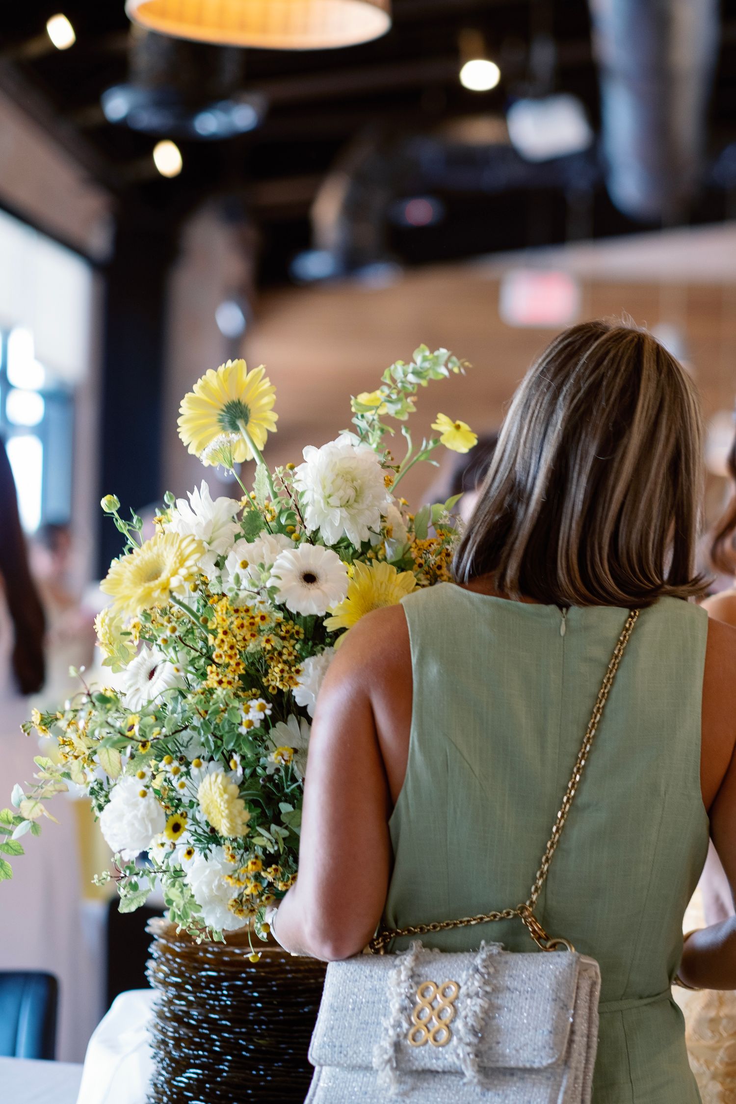 Woman in mint green dress sits at table with yellow and white floral centerpiece arrangements.