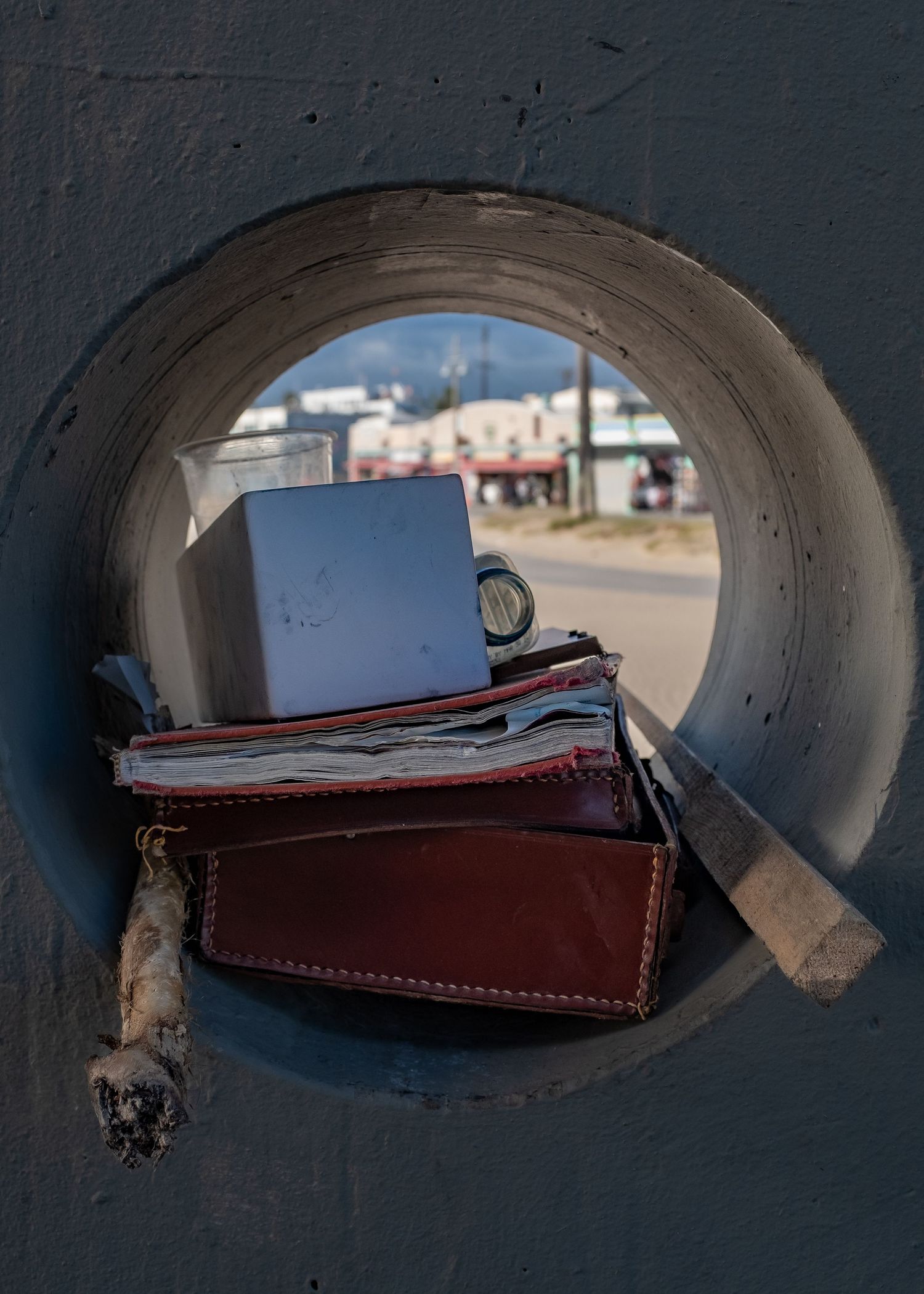 A leather wallet and documents rest inside a circular concrete opening with a street scene visible in the background.