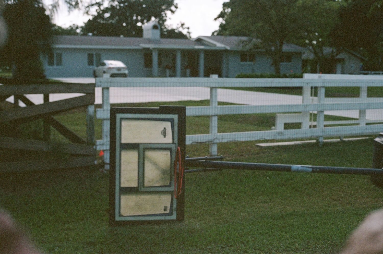 A framed window leaning against a white wooden fence near a blue house on a green lawn.